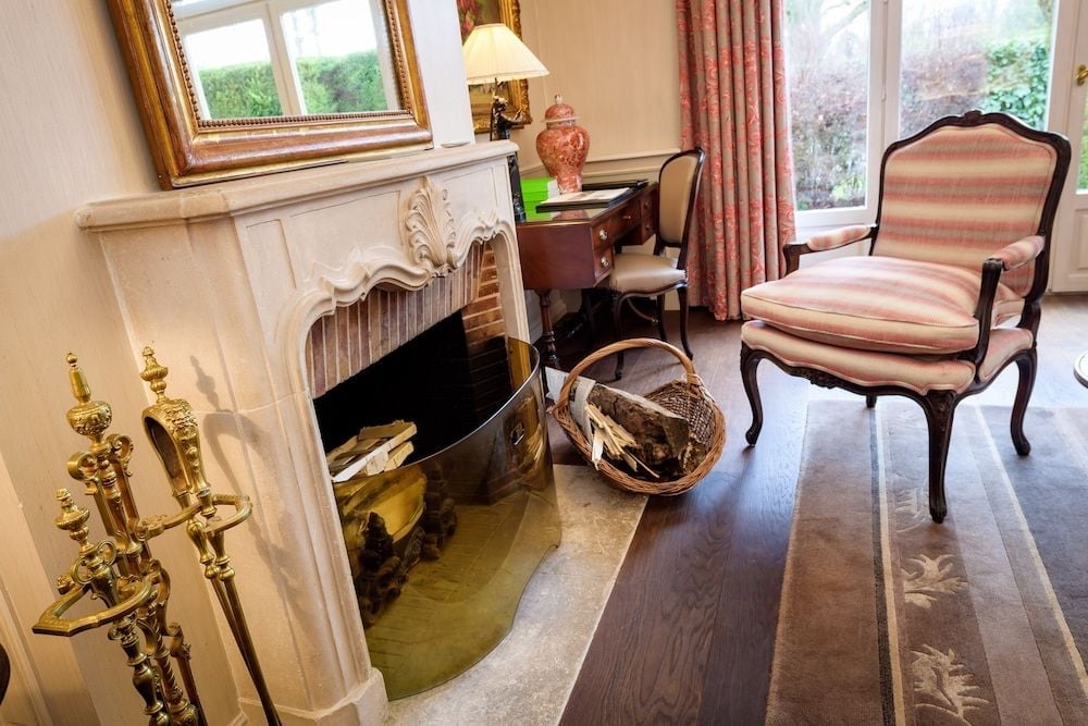 Ornate brass fireplace tools catch afternoon light streaming through tall windows, while striped silk armchairs invite intimate conversations beside the crackling hearth.