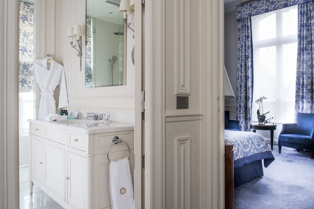 Elegant white cabinetry and blue toile wallpaper create a sophisticated en-suite vanity, where plush robes await and glimpses of the adjoining bedroom beckon.