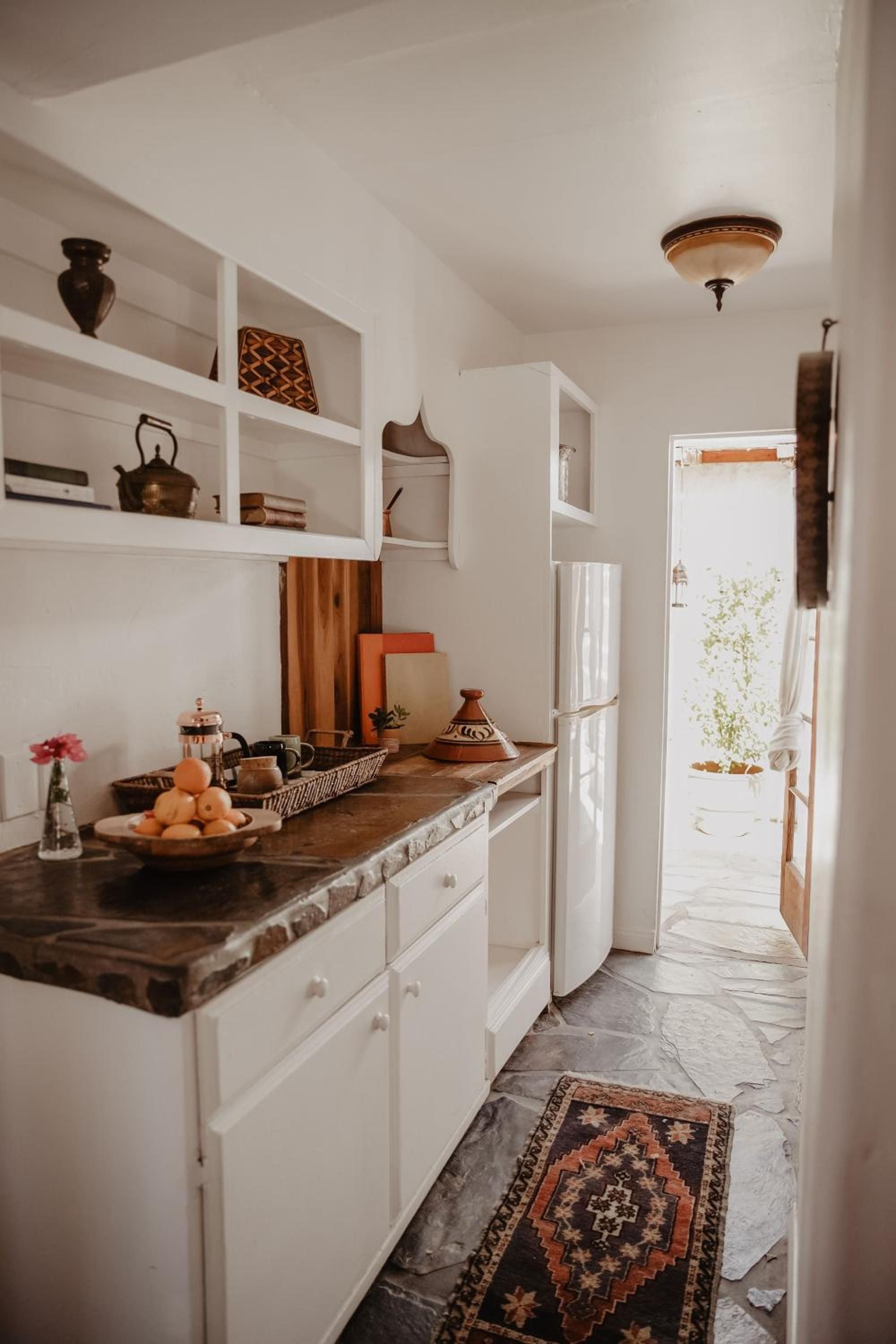 Moroccan ceramics and vintage brass fill open shelving in this sun-drenched galley kitchen, where terracotta tagines hint at North African culinary adventures ahead.