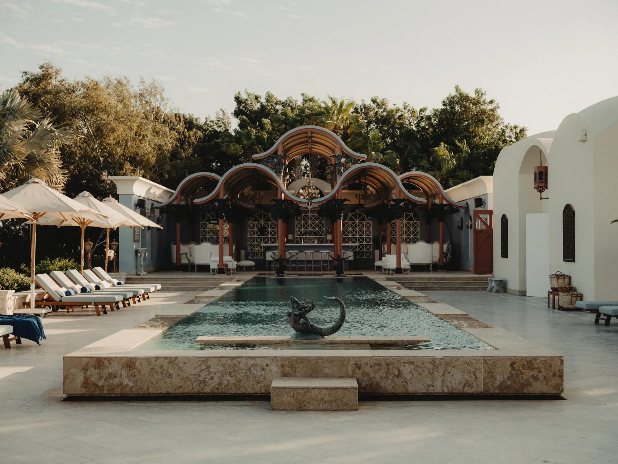 Moorish-inspired arches frame the central courtyard pool, where sculptural elements and honey-colored stonework create an intimate oasis beneath swaying palms.