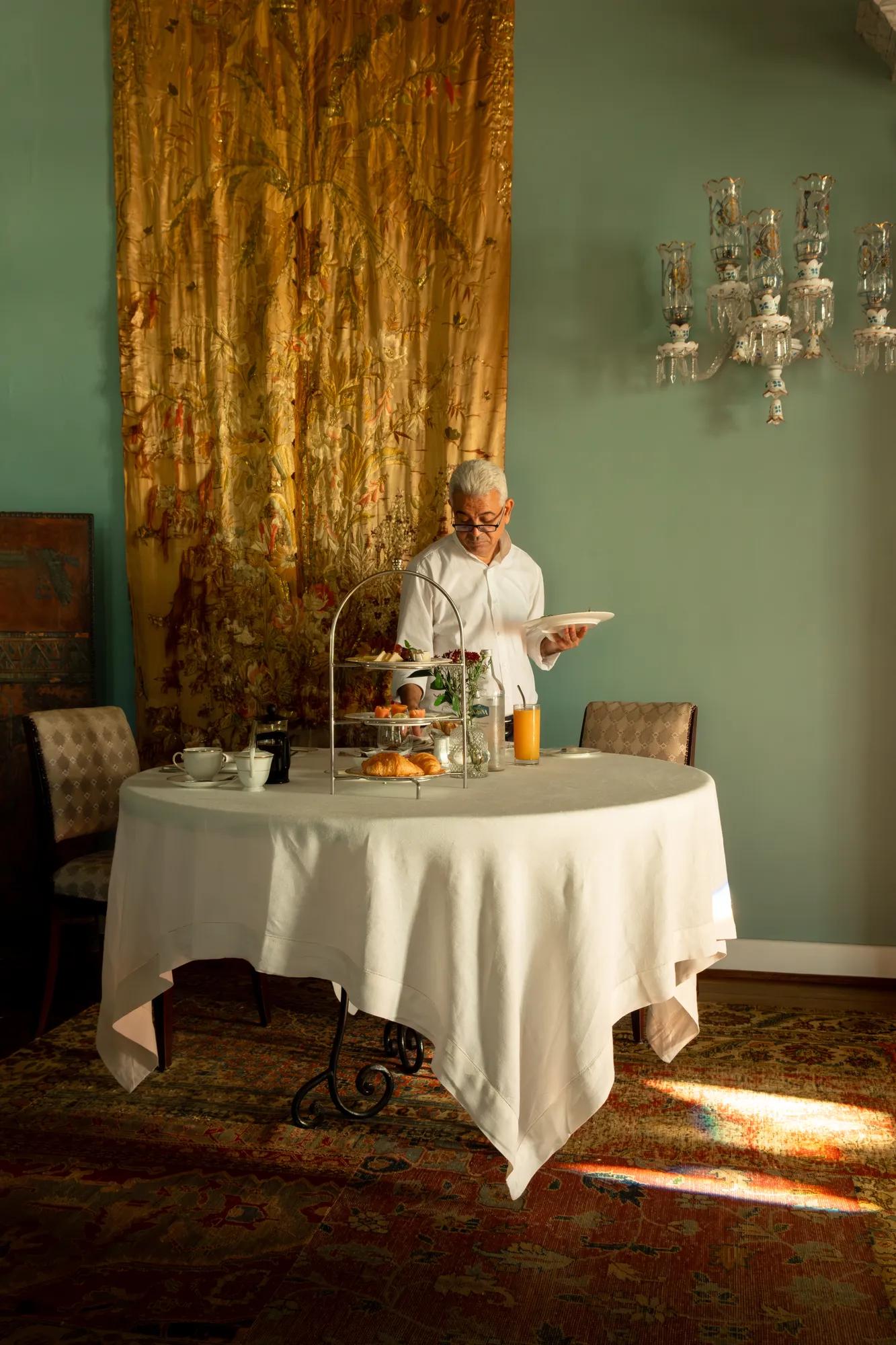 Morning light filters through silk tapestries as breakfast arrives on silver stands, transforming this sage-walled salon into an intimate theater of Moroccan hospitality.