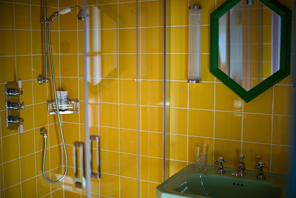 Vintage charm meets modern convenience in this cheerful yellow-tiled bathroom, where an emerald green sink and octagonal mirror create playful retro elegance.