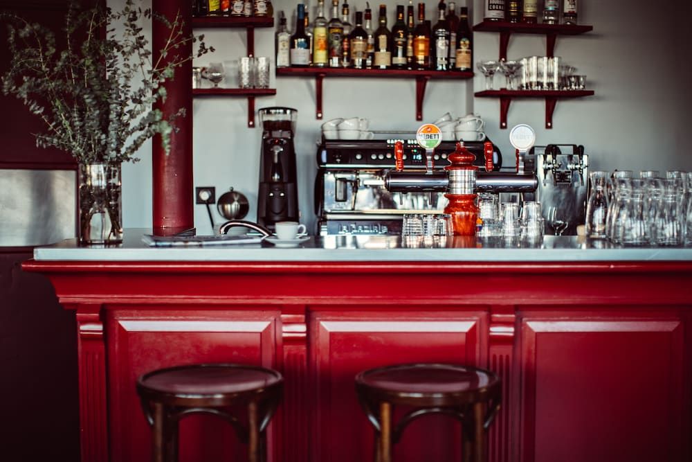 Rich burgundy woodwork frames the intimate bar, where polished brass fixtures catch warm light beneath shelves lined with premium spirits and glassware.