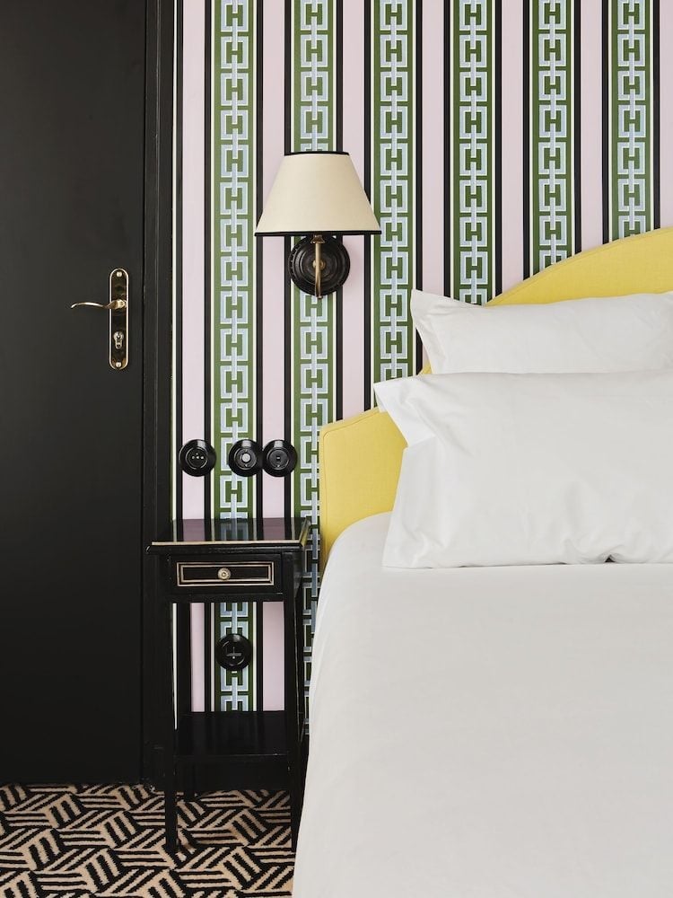 Geometric wallpaper in sage and plum frames crisp white linens accented with sunny yellow pillows, while a brass-detailed bedside lamp casts intimate light.