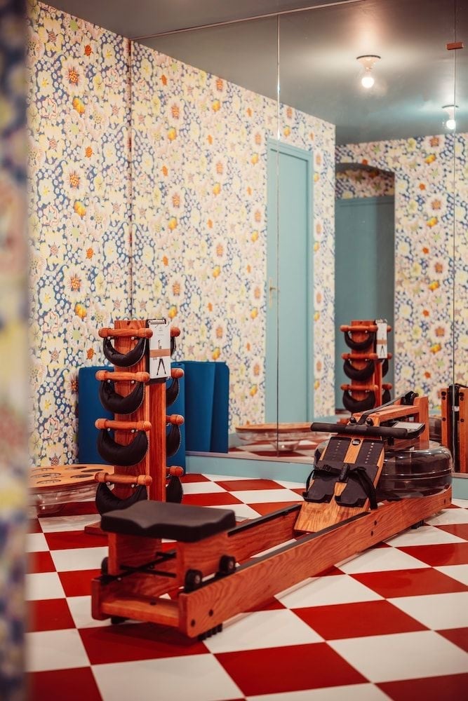Vintage wooden rowing machines and leather equipment pods create an unexpectedly stylish workout space beneath colorful mosaic tiles and red-checkered floors.