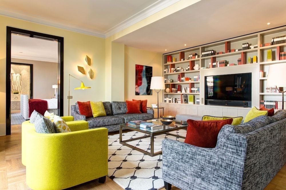 Vibrant chartreuse chairs pop against textured gray sofas in this sophisticated suite, where floor-to-ceiling bookshelves frame a sleek entertainment center and geometric rugs anchor the refined living space.
