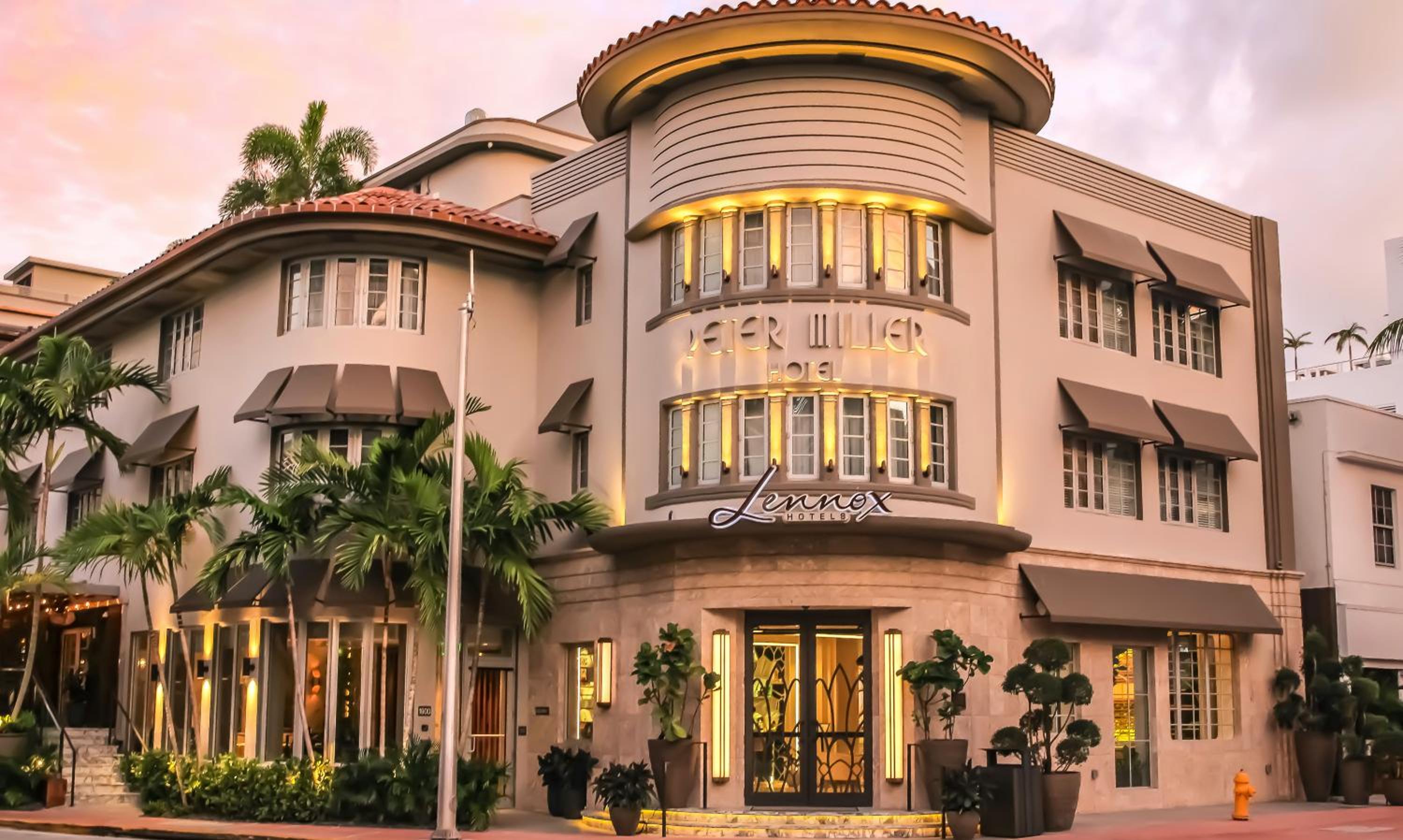 Art Deco curves and coral-hued stucco catch Miami's golden hour light, while palm fronds frame the boutique hotel's signature cylindrical tower and welcoming entrance.