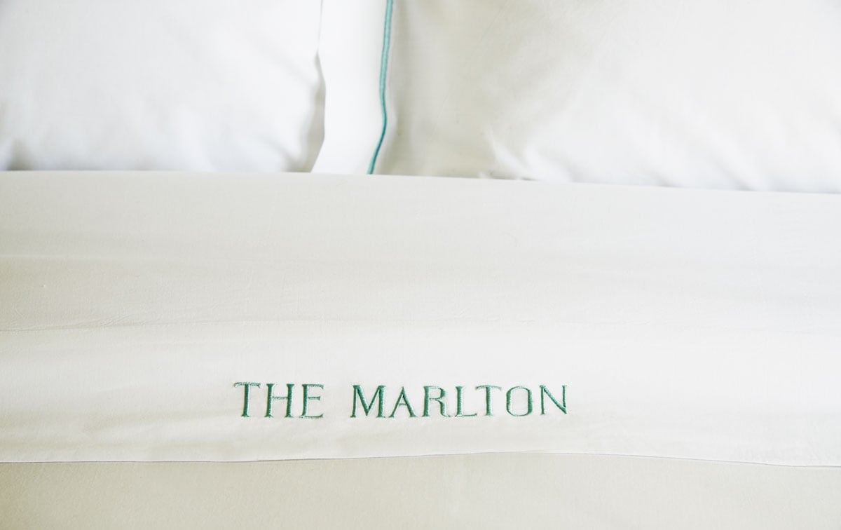 Crisp white linens embroidered with the hotel's name in sage green lettering create an intimate, personalized touch that whispers luxury without shouting.