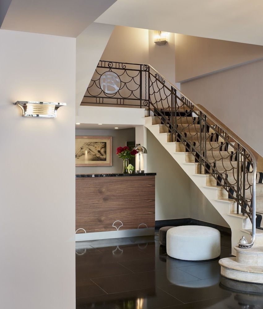 Graceful wrought-iron railings with scalloped motifs frame the curved staircase, while warm sconces cast golden light across polished stone steps and rich walnut millwork.