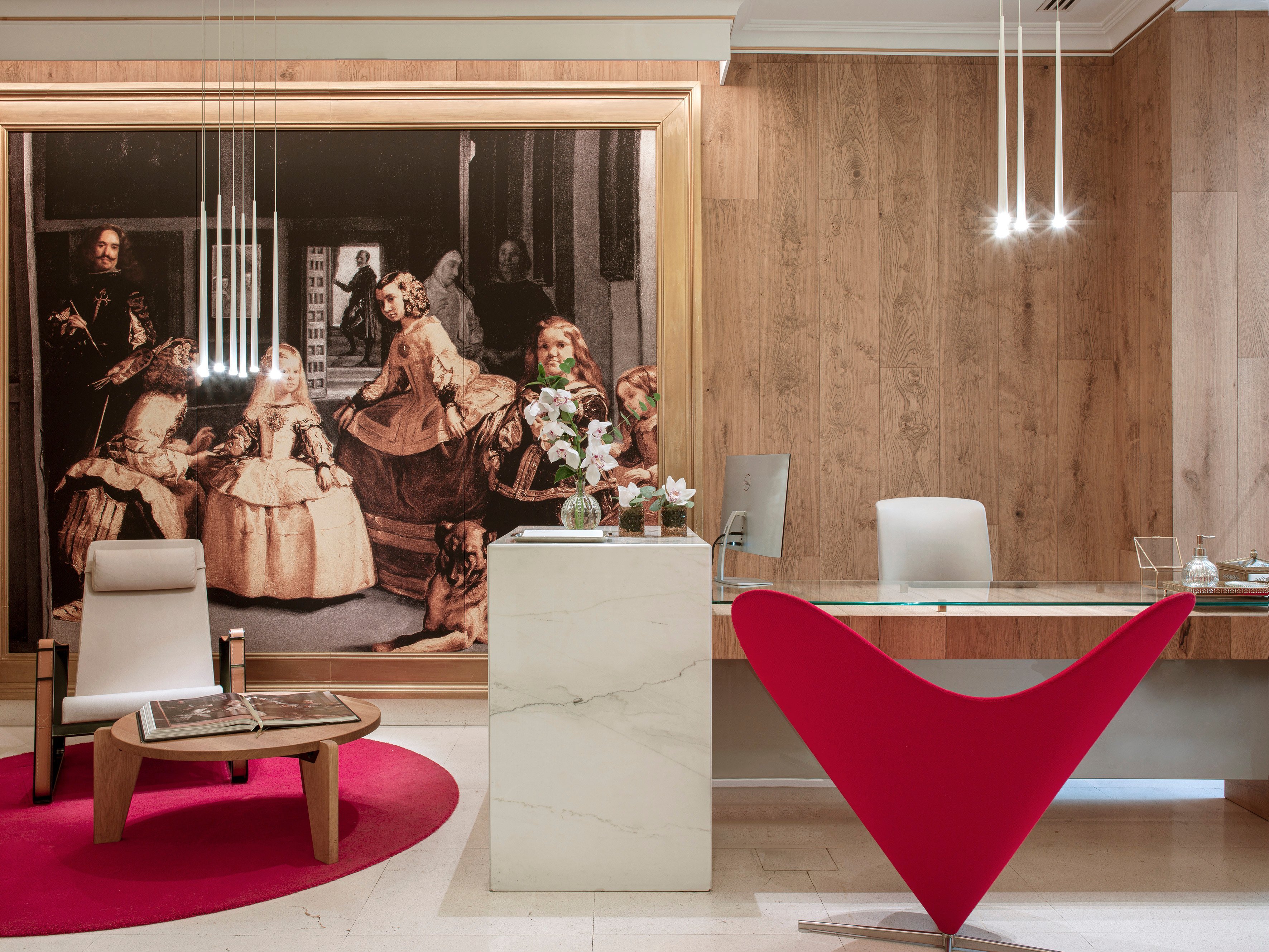 Bold crimson furnishings pop against warm wood paneling and classical art in this striking Madrid lobby, where Velázquez-inspired murals meet contemporary Danish design.