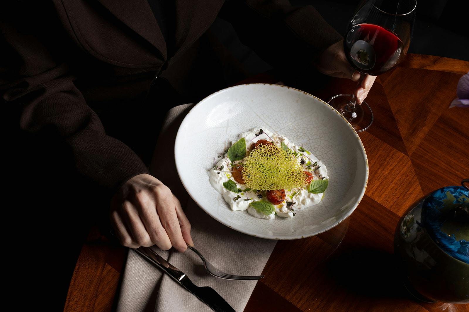 Artfully plated dessert crowned with vibrant green pistachio dust catches warm candlelight, while rich red wine awaits—fine dining elevated to theater at this sophisticated Stockholm table.