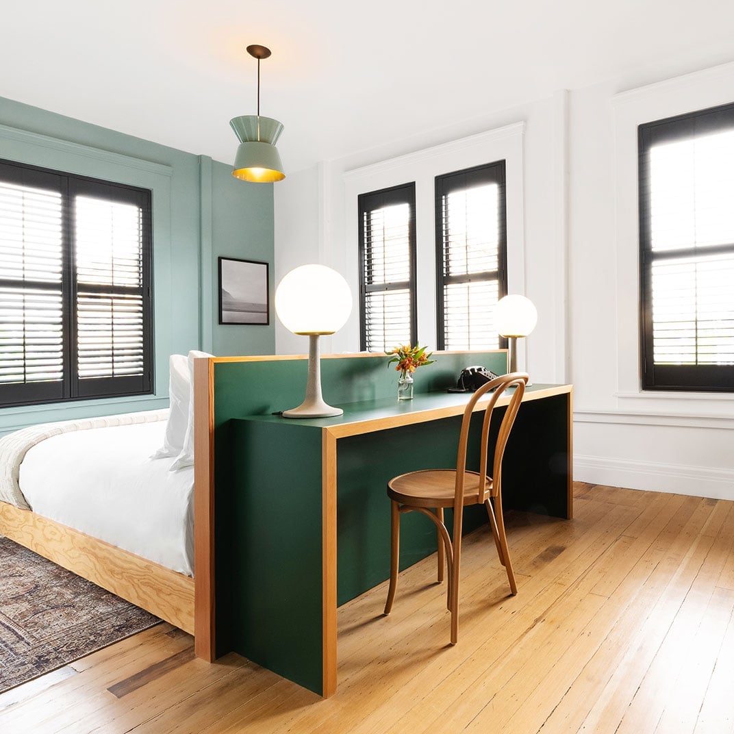Sage green accent walls and warm wood floors create an intimate workspace within this thoughtfully designed studio, where modern pendant lights cast a golden glow over the built-in desk.