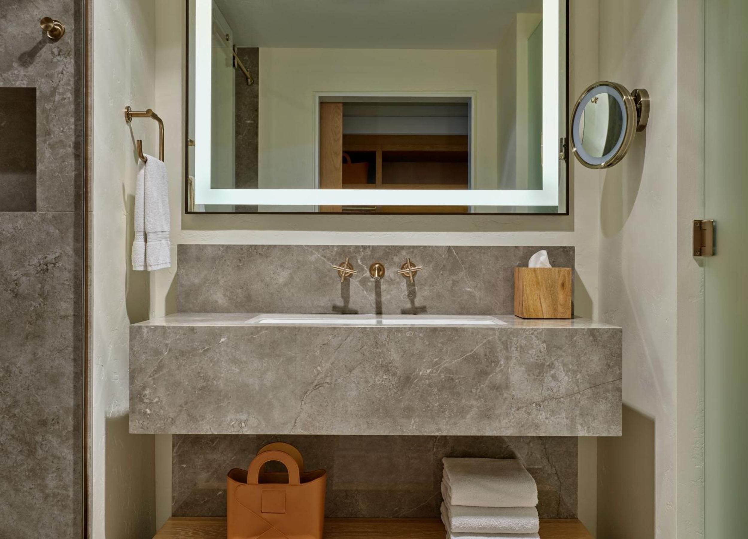 Warm brass fixtures and travertine surfaces create a spa-like sanctuary, where natural stone meets modern minimalism in this thoughtfully appointed guest bathroom.