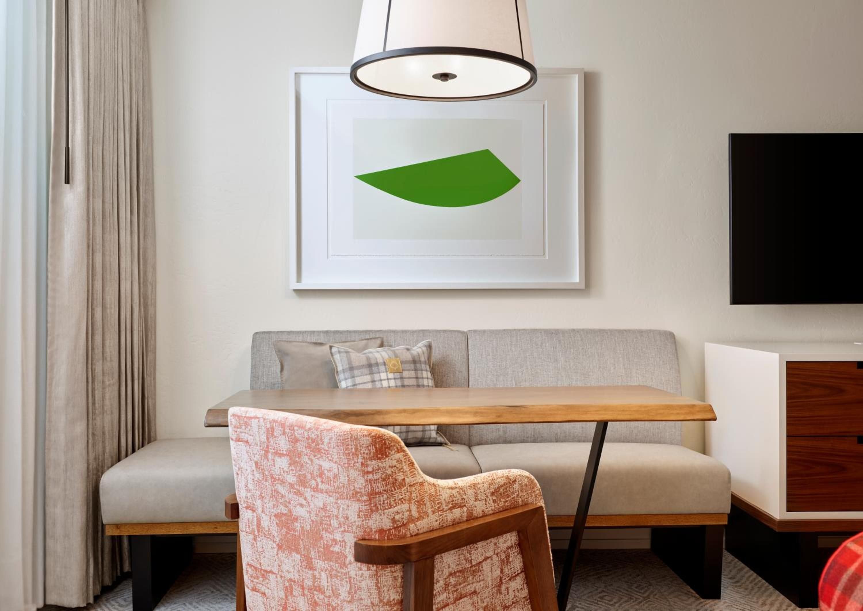 Natural wood meets modern comfort in thoughtfully appointed guest rooms, where a circular pendant light casts warm ambiance over the intimate dining nook's plush banquette seating.