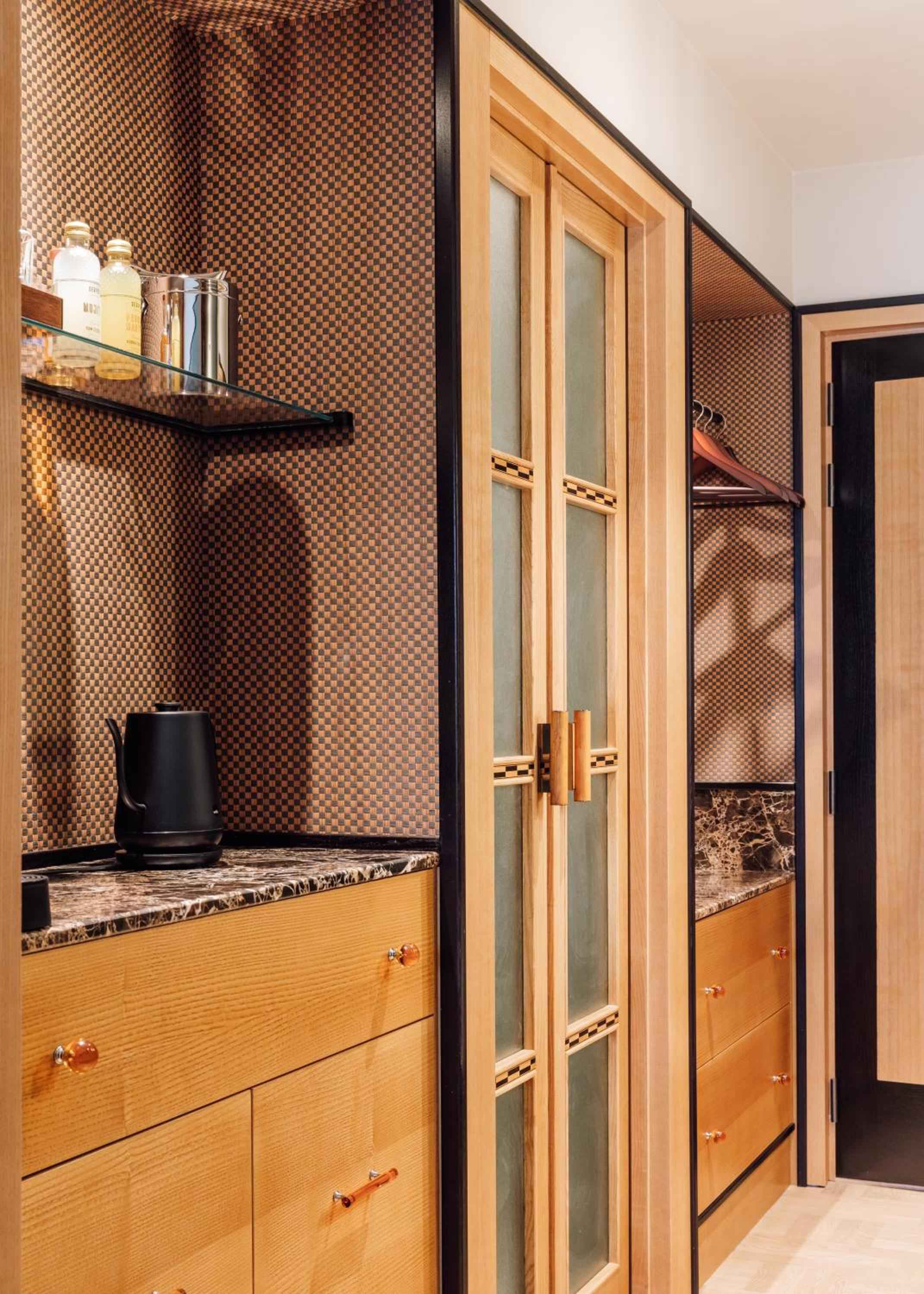 Warm oak cabinetry and rich marble countertops create an intimate galley kitchen, where geometric wallpaper adds sophisticated texture to this thoughtfully appointed space.