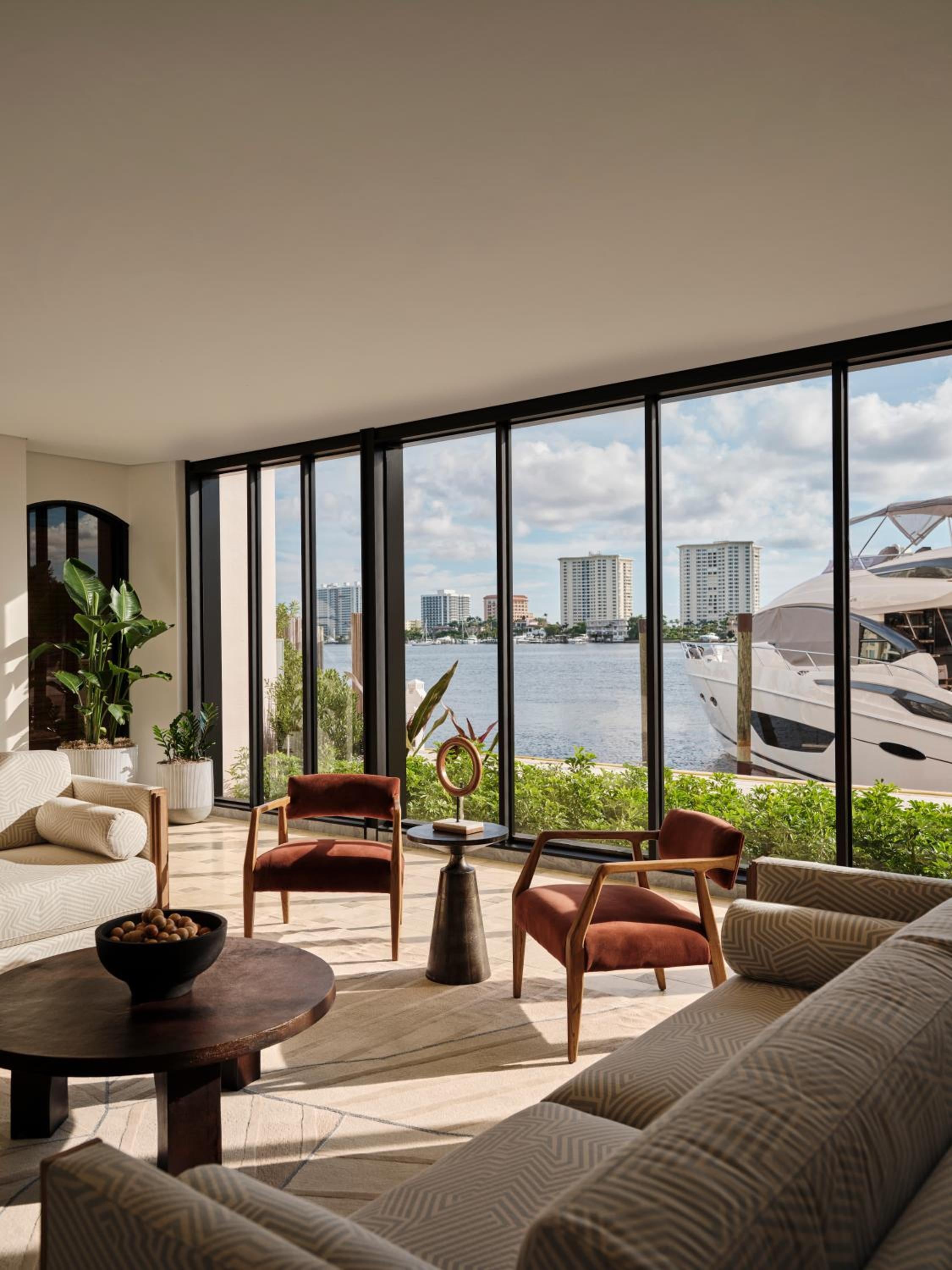 Floor-to-ceiling windows frame the Intracoastal Waterway from this sophisticated suite, where burnt orange chairs and tropical plantings create an elegant sanctuary overlooking bobbing yachts and distant towers.