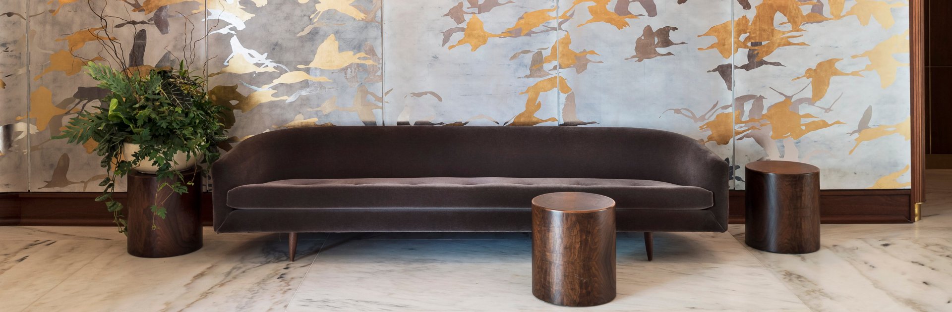Curved charcoal velvet banquettes face hand-painted murals of migrating birds, while polished wood drums anchor this sophisticated lobby lounge with understated elegance.