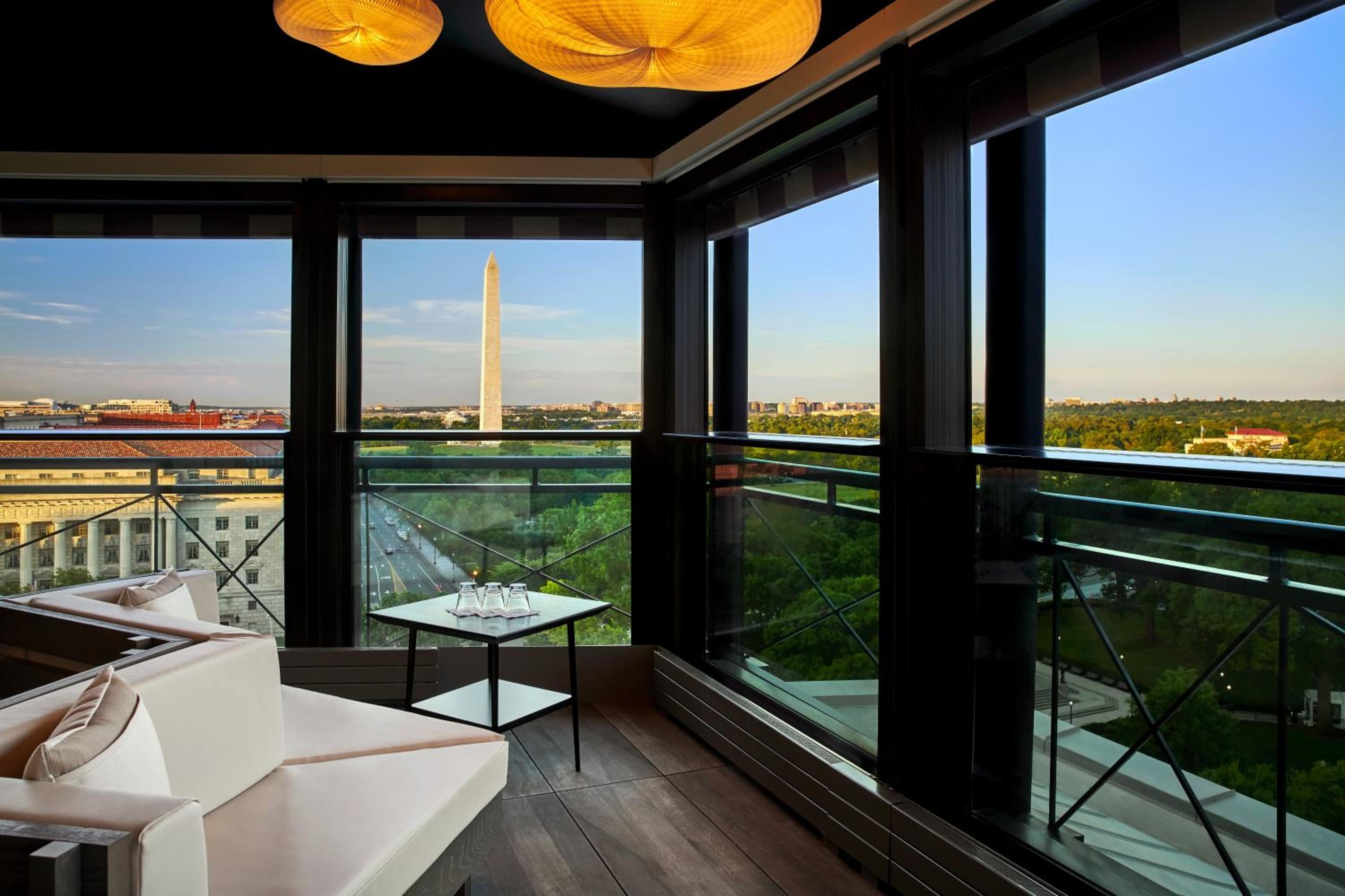 Golden pendant lights cast a warm glow over plush seating while the Washington Monument pierces the horizon through floor-to-ceiling windows at this elevated perch.