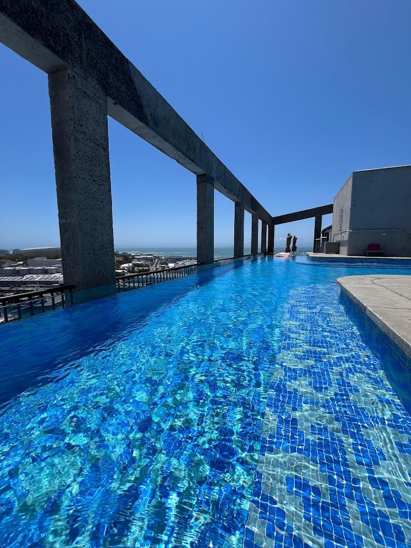 Brilliant blue mosaic tiles shimmer beneath concrete columns as Cape Town's coastline stretches beyond this striking rooftop infinity pool sanctuary.