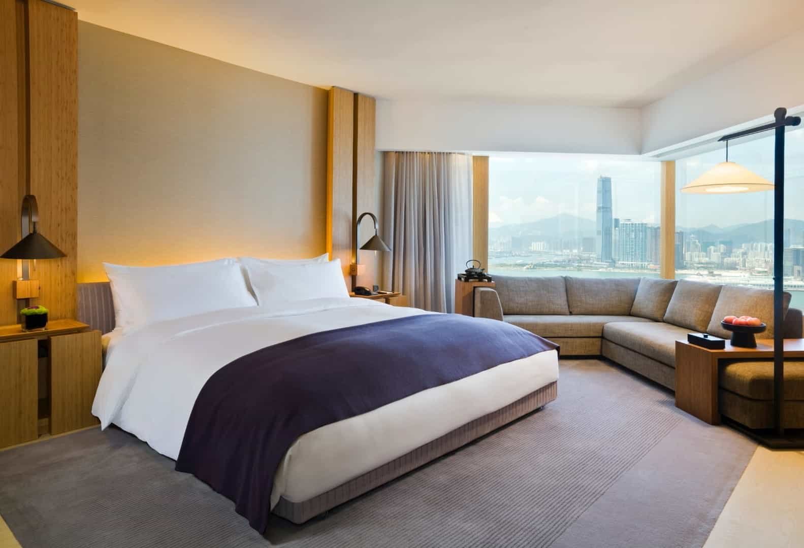 Floor-to-ceiling windows frame Victoria Harbour's glittering skyline while warm wood tones and plush furnishings create an intimate sanctuary above Hong Kong's urban energy.