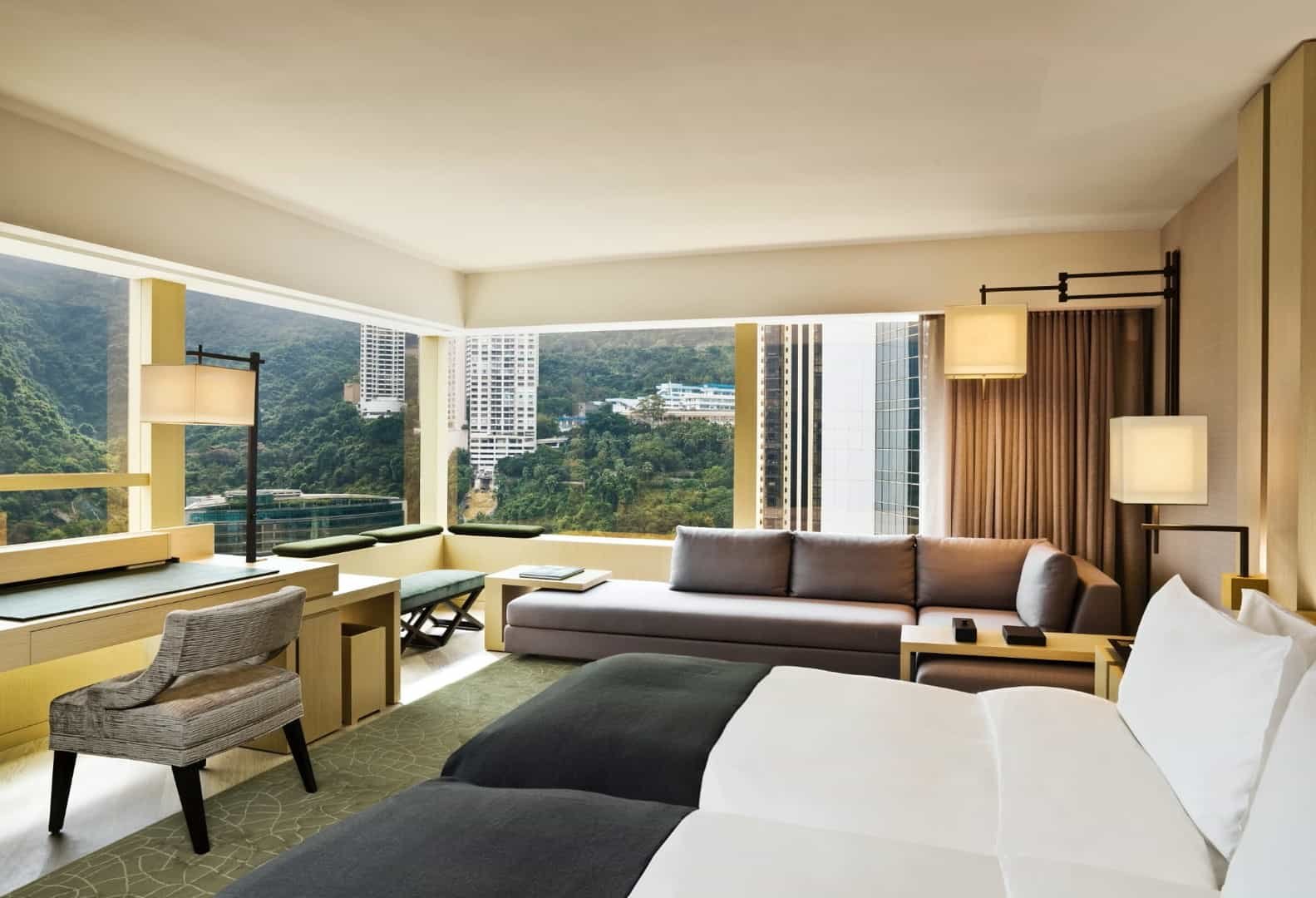 Floor-to-ceiling windows frame Hong Kong's verdant hills from this serene suite, where warm wood tones and tailored furnishings create an urban sanctuary above the bustling city.