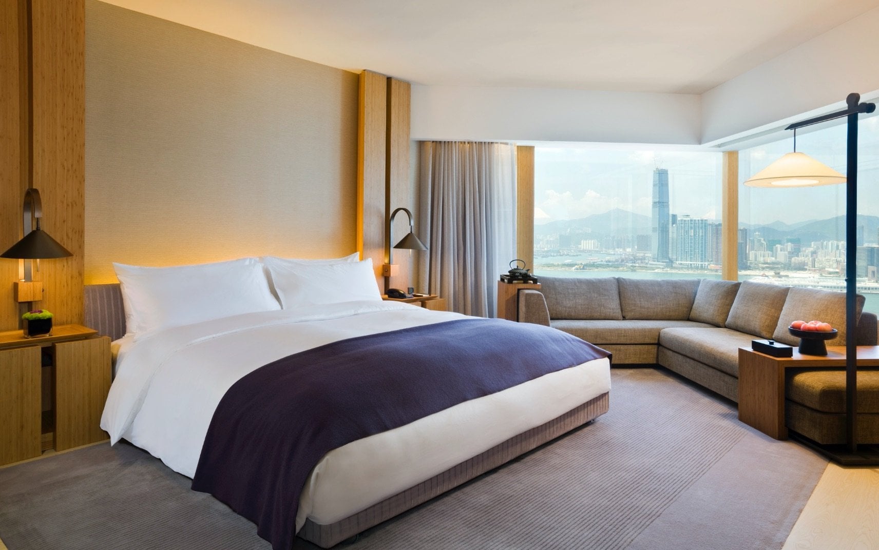 Floor-to-ceiling windows frame Hong Kong's glittering skyline while warm wood paneling and plush neutrals create an intimate sanctuary high above the bustling city below.