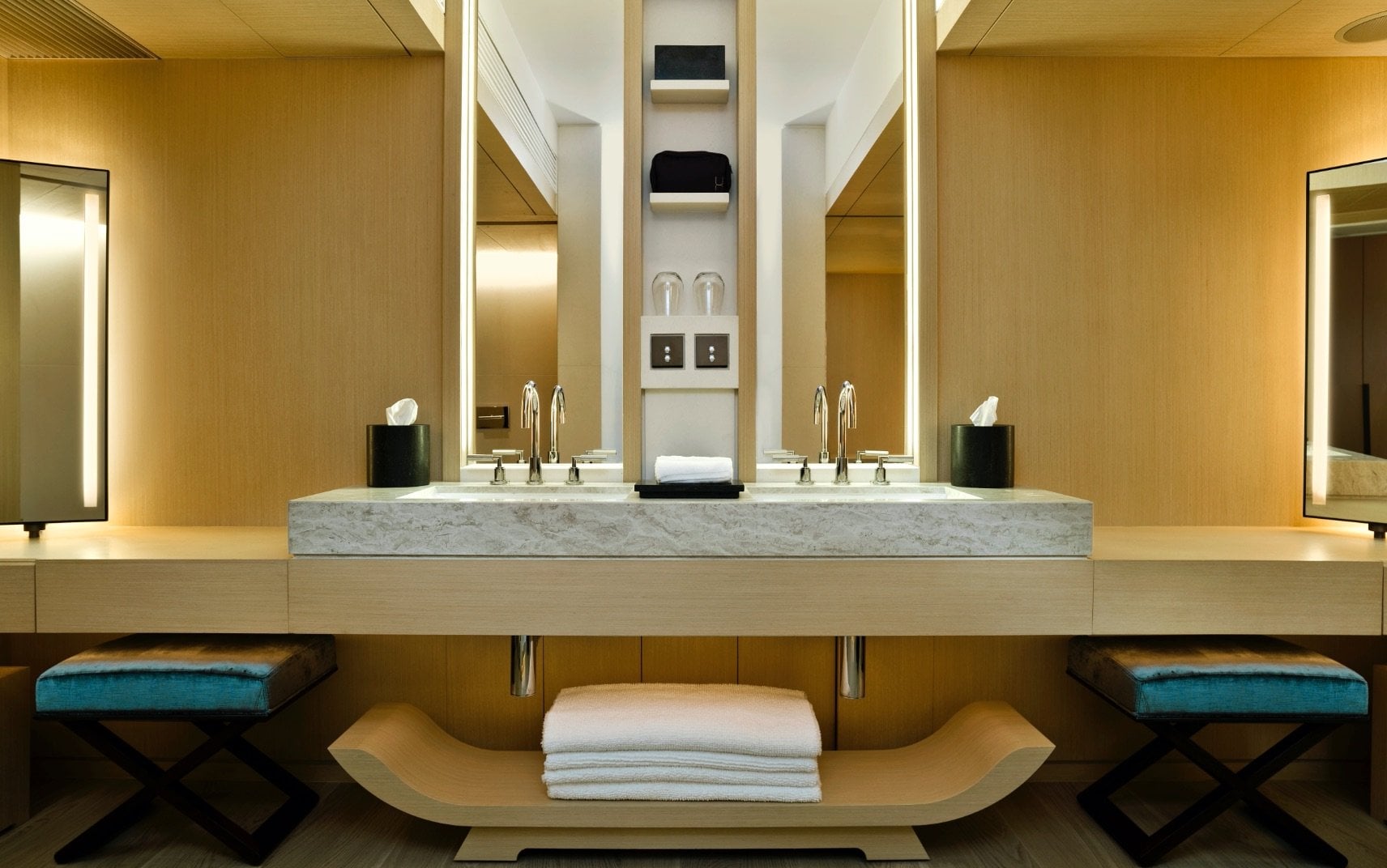 Warm wood tones and marble create a spa-like sanctuary, where thoughtful details like teal velvet stools and perfectly folded towels elevate the daily ritual.