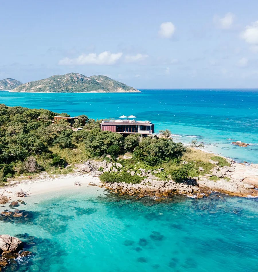 Crystalline waters lap at pristine shores where contemporary pavilions nestle into verdant hillsides, offering unobstructed views across the Great Barrier Reef's turquoise expanse.
