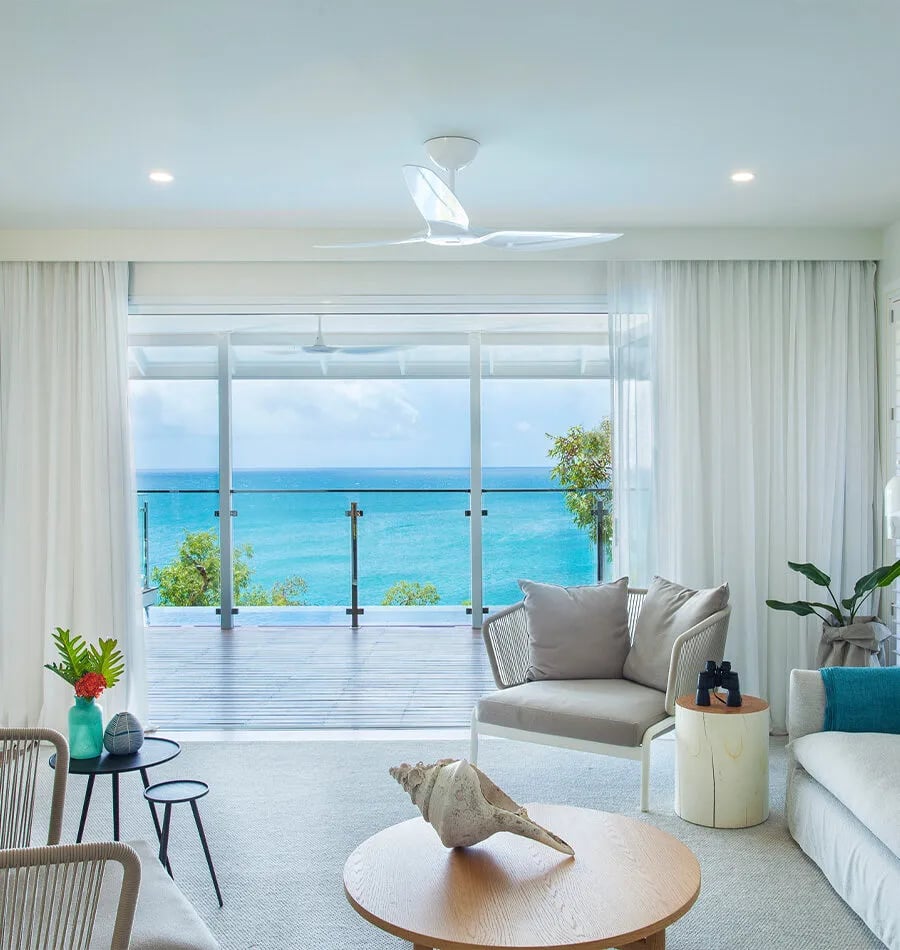 Floor-to-ceiling windows frame the Coral Sea's brilliant turquoise from this suite's sanctuary, where white linens and natural textures echo the island's serene coastal palette.