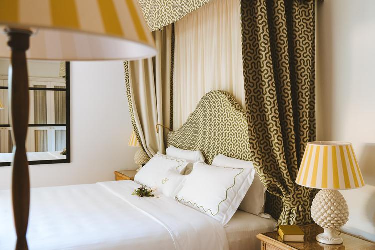 Geometric patterned headboards and matching drapery create intimate cocoons of luxury, while striped lampshades cast warm golden light across crisp Italian linens.