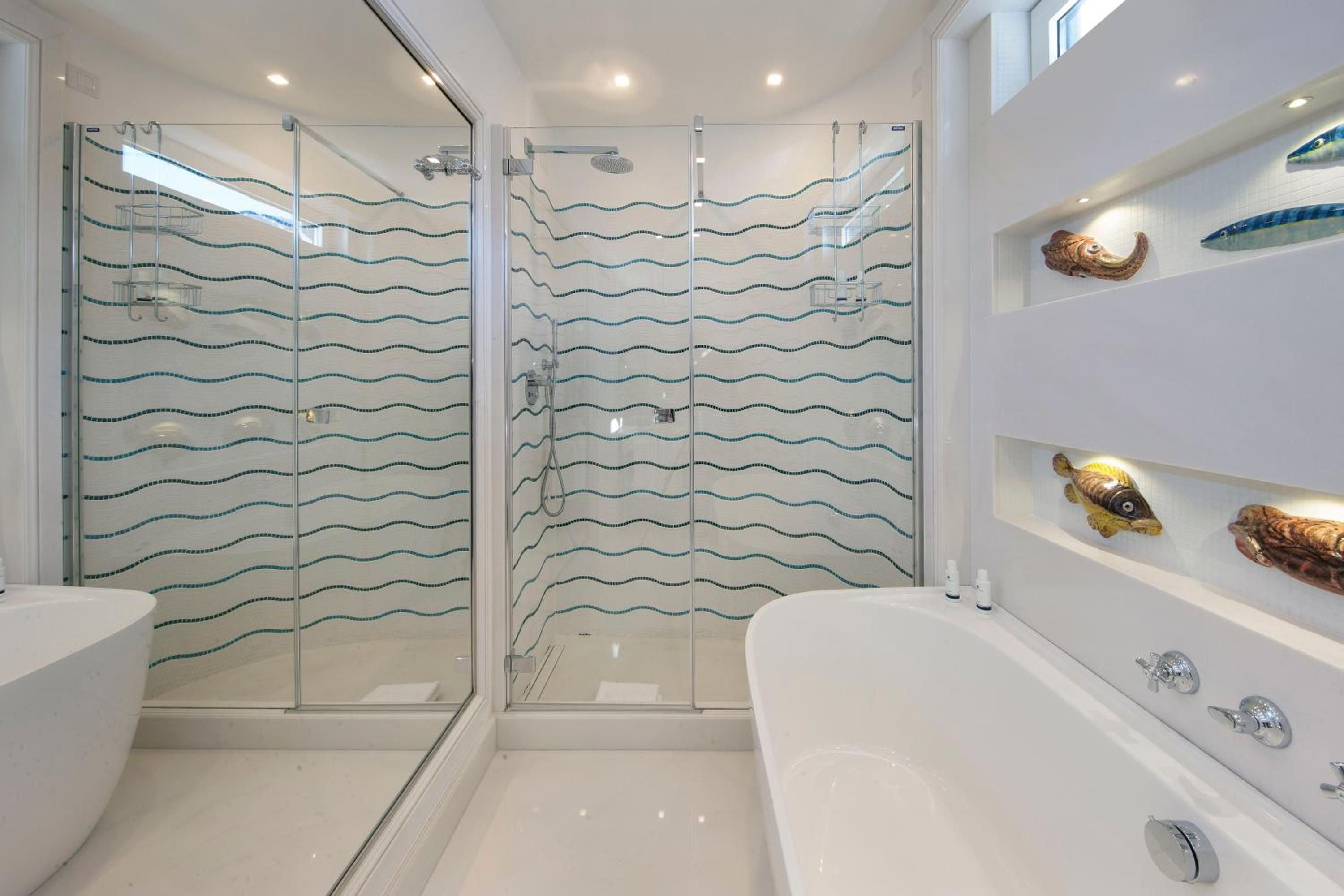 Wave-patterned mosaic tiles echo the Amalfi coastline in this spa-like suite bathroom, where polished marble and glass create a serene sanctuary above the sea.