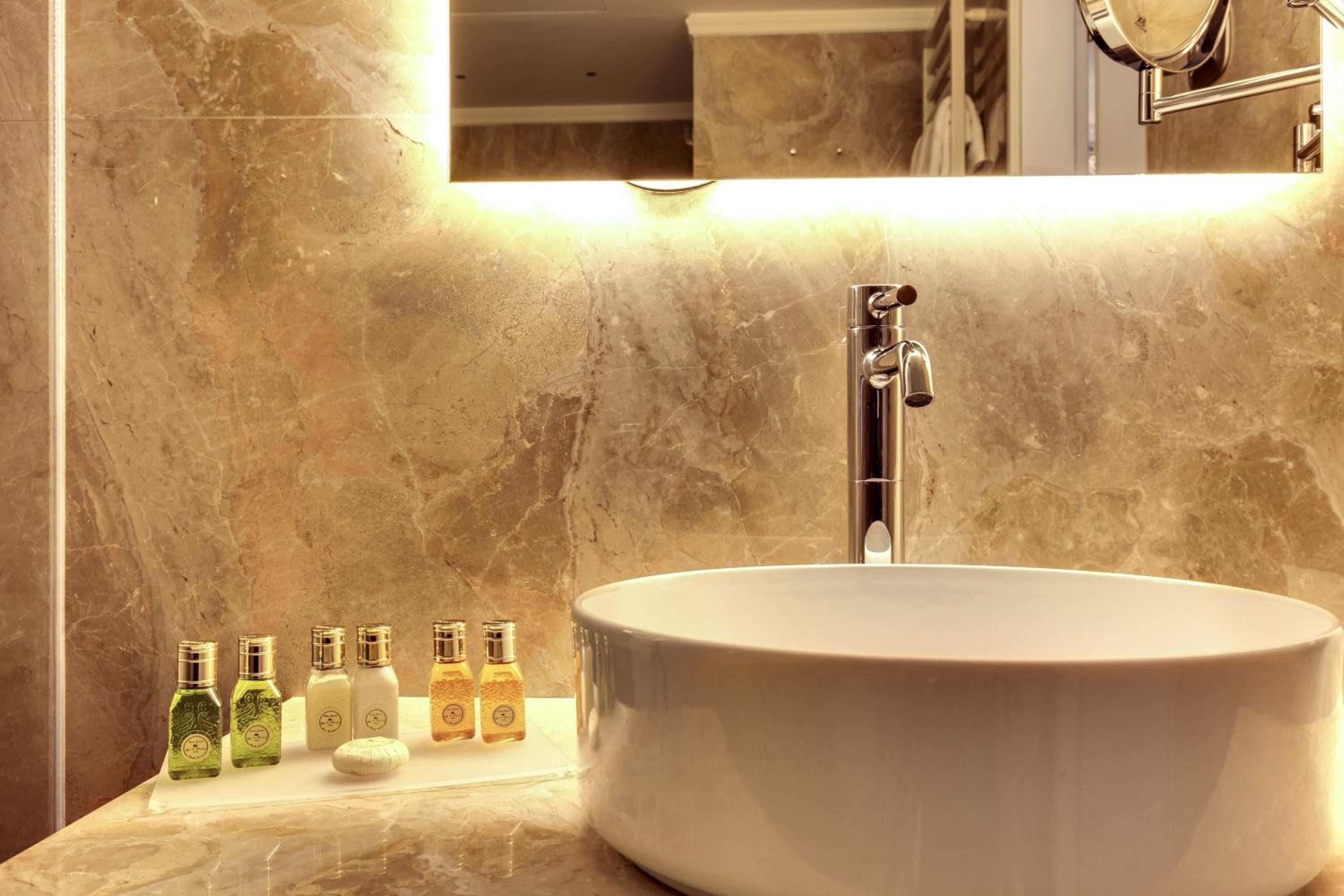 Warm marble embraces a sculptural basin where thoughtfully curated amenities await, while hidden lighting transforms this intimate powder room into a serene sanctuary.