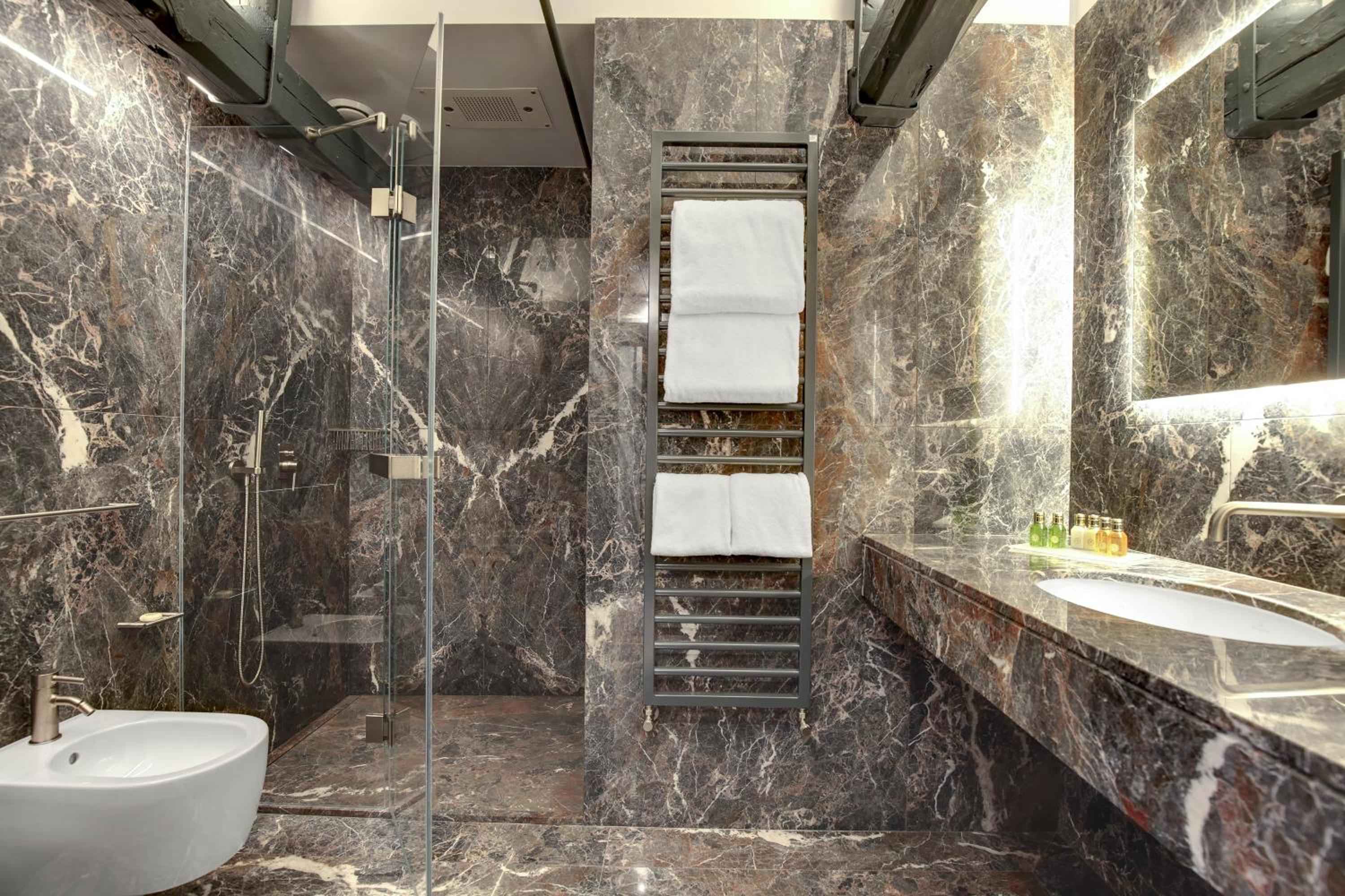 Dramatic veined marble creates an opulent cocoon in this suite bathroom, where warm lighting plays across stone surfaces and plush towels await on heated rails.