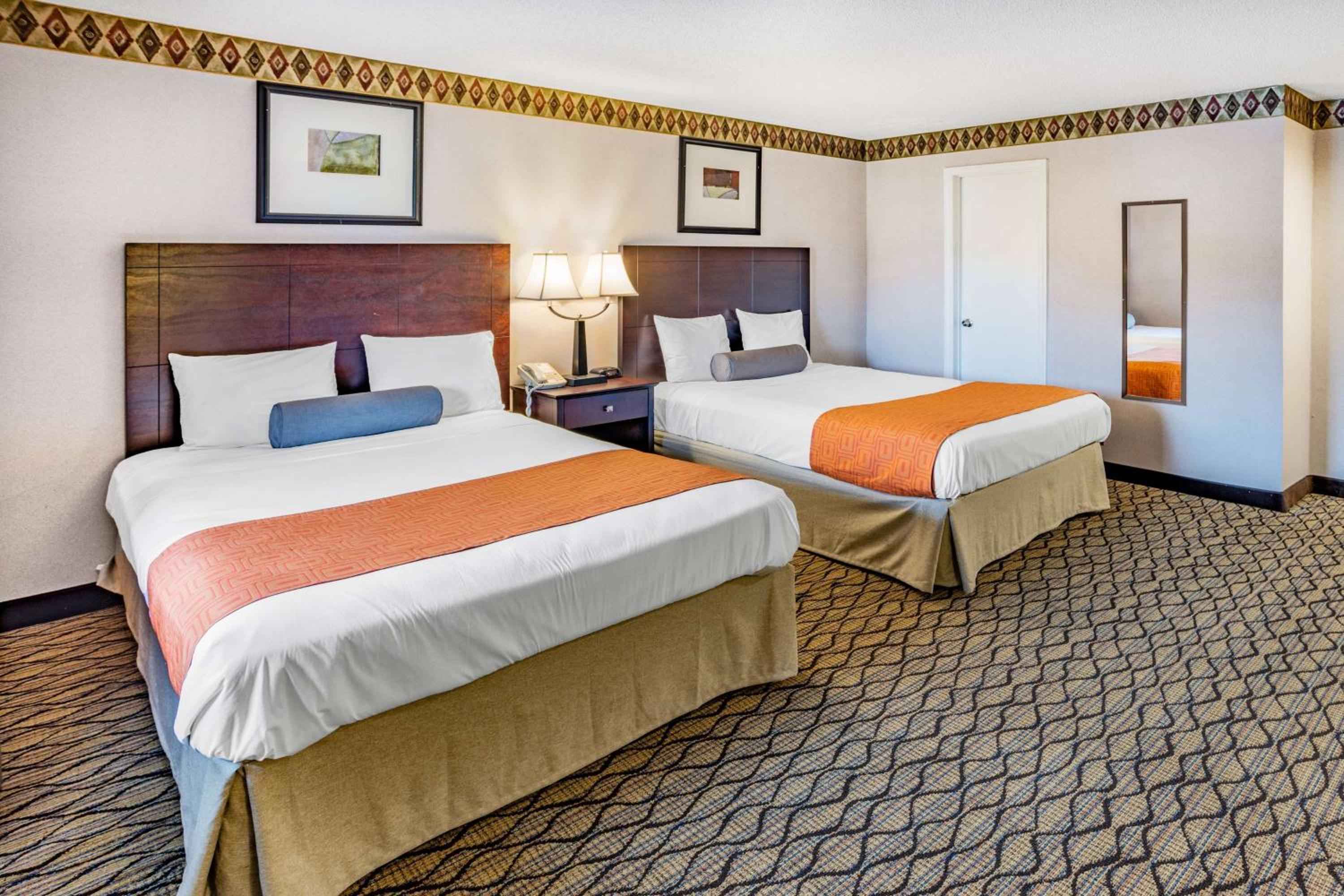 Twin beds with warm wood headboards and geometric carpet create a cozy retreat, while diamond-patterned wallpaper borders add Southwest-inspired charm to this comfortable double room.
