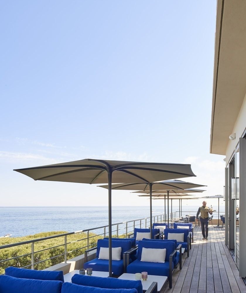 Blue cushioned seating beneath crisp umbrellas creates an intimate terrace dining experience, where Mediterranean breezes carry the scent of sea air across weathered decking.