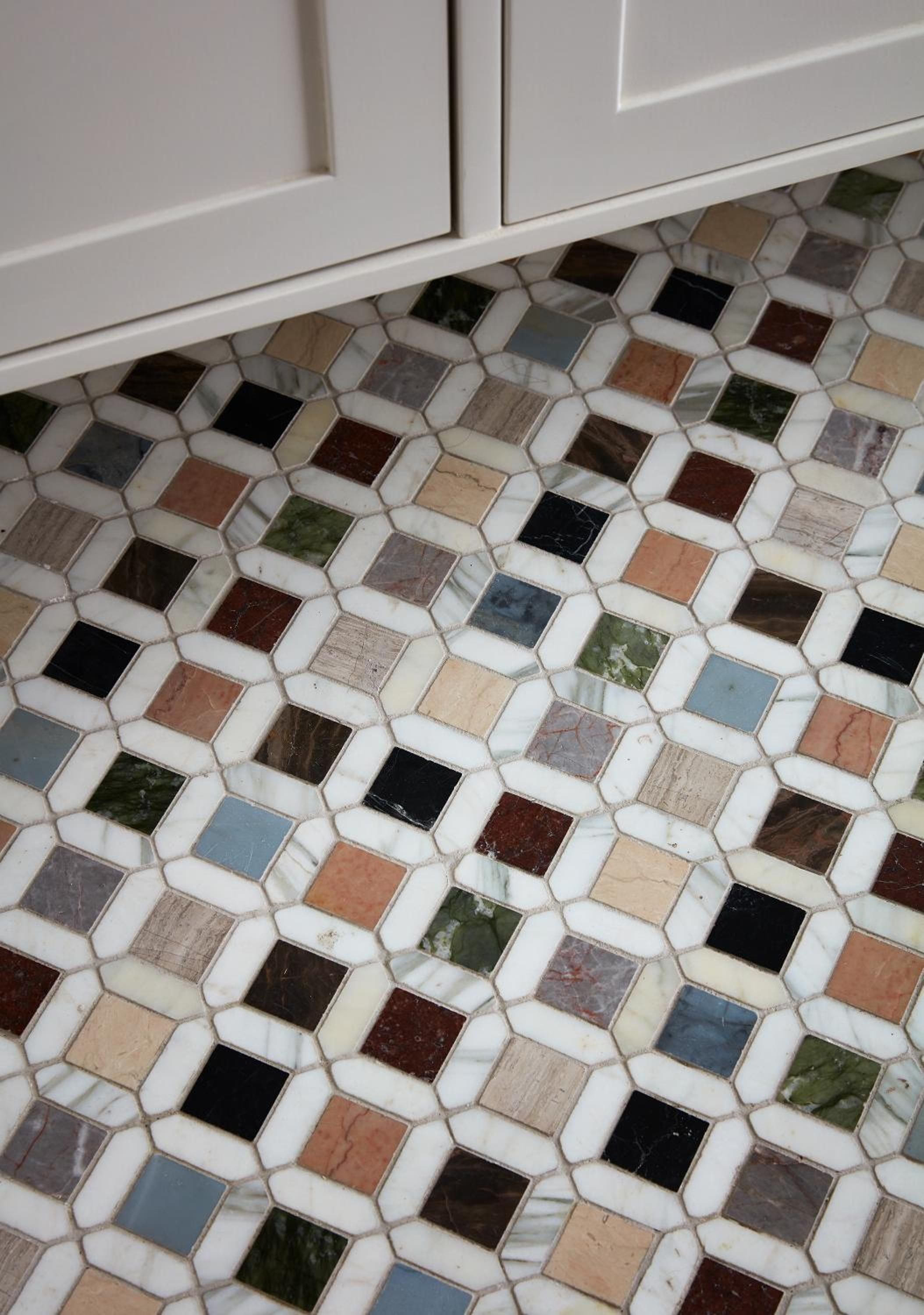 Mosaic tiles in earthy greens, blues, and terracotta create an intricate geometric pattern beneath crisp white cabinetry, showcasing artisanal craftsmanship in every carefully placed stone.