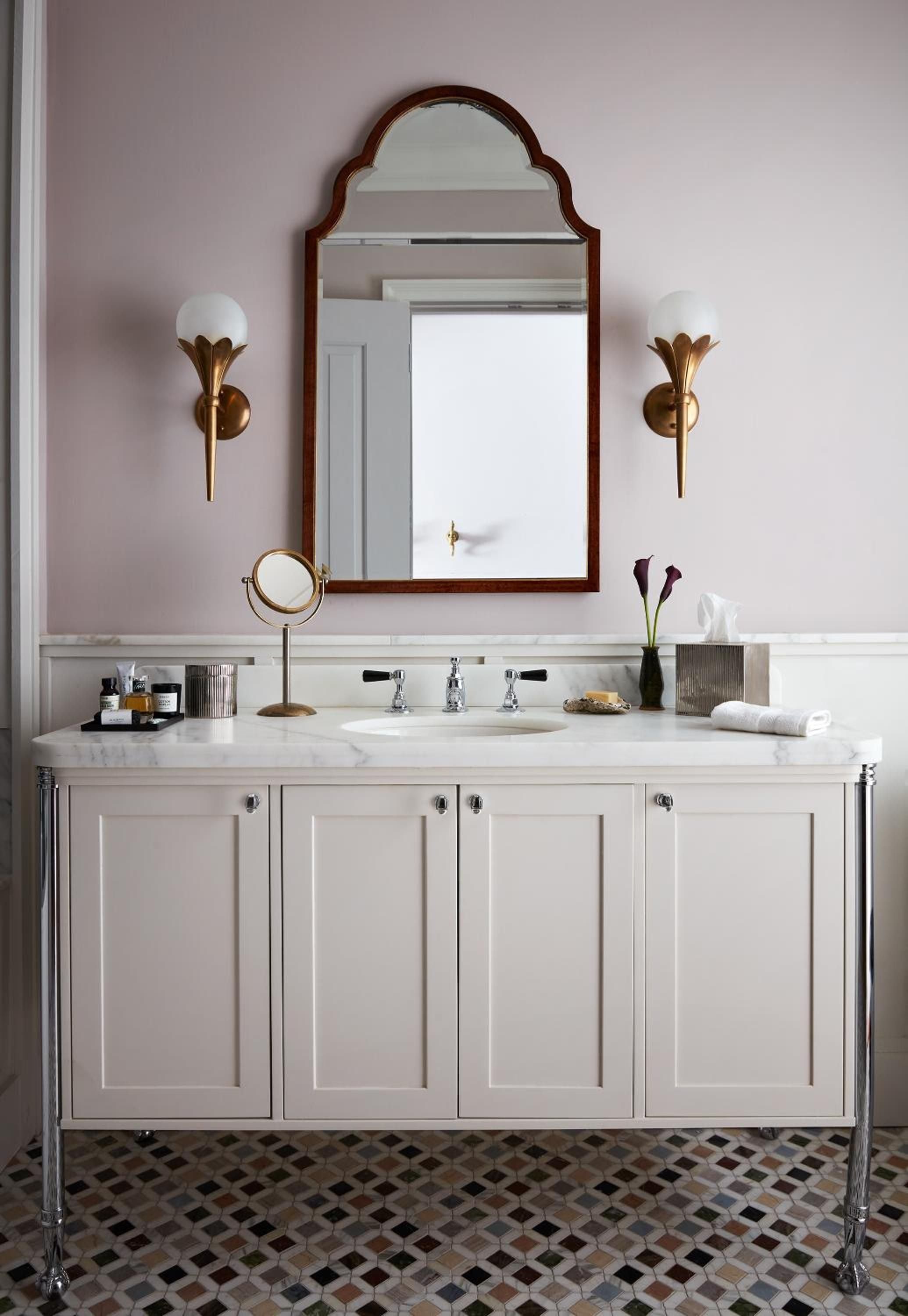 Brass sconces cast a warm glow over marble countertops and mosaic floors, where vintage meets modern in this thoughtfully appointed powder room.