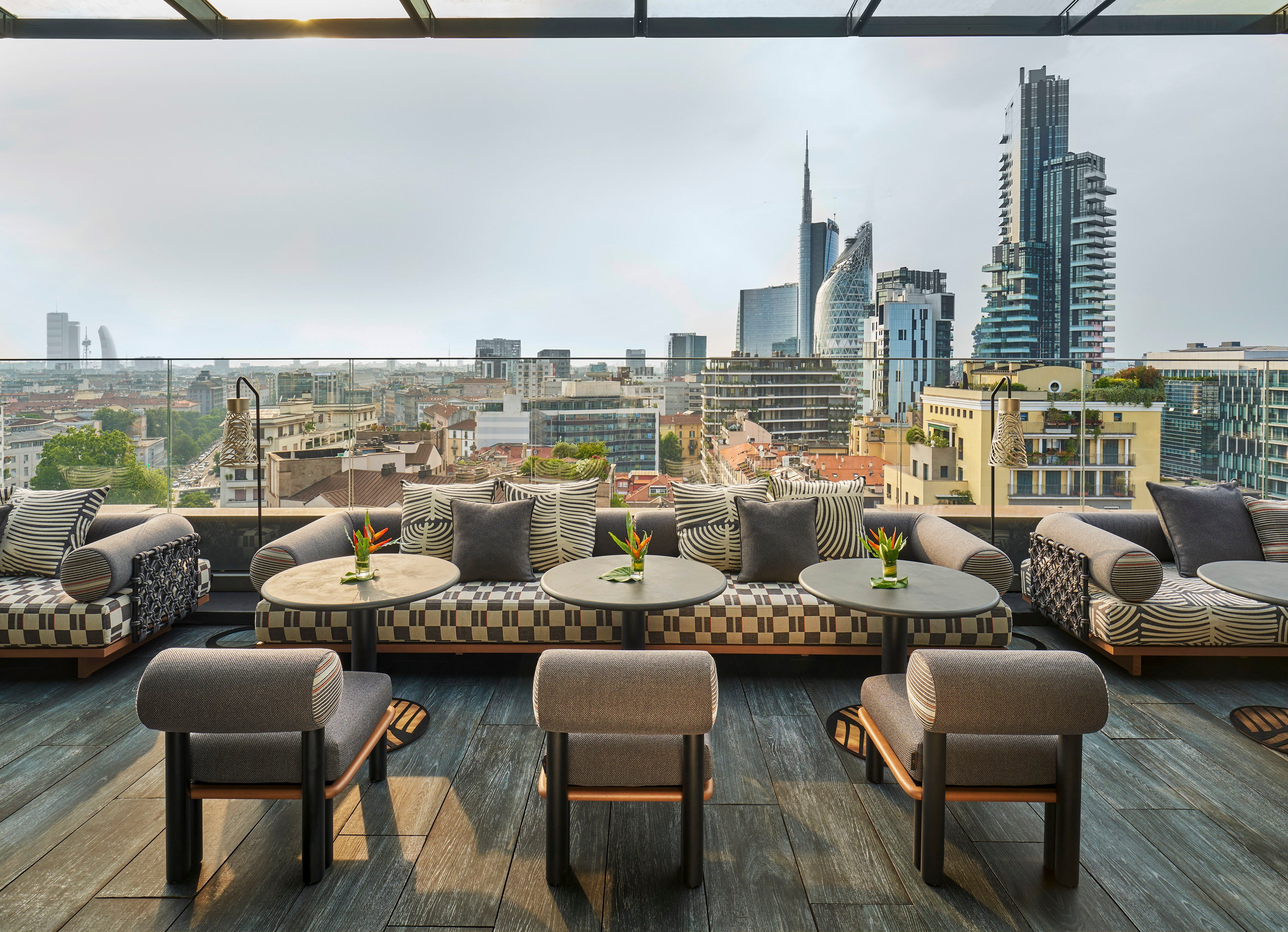 Geometric cushions and bird-of-paradise blooms frame Milan's evolving skyline from this sophisticated rooftop terrace, where modern towers rise beyond terracotta-tiled neighborhoods.