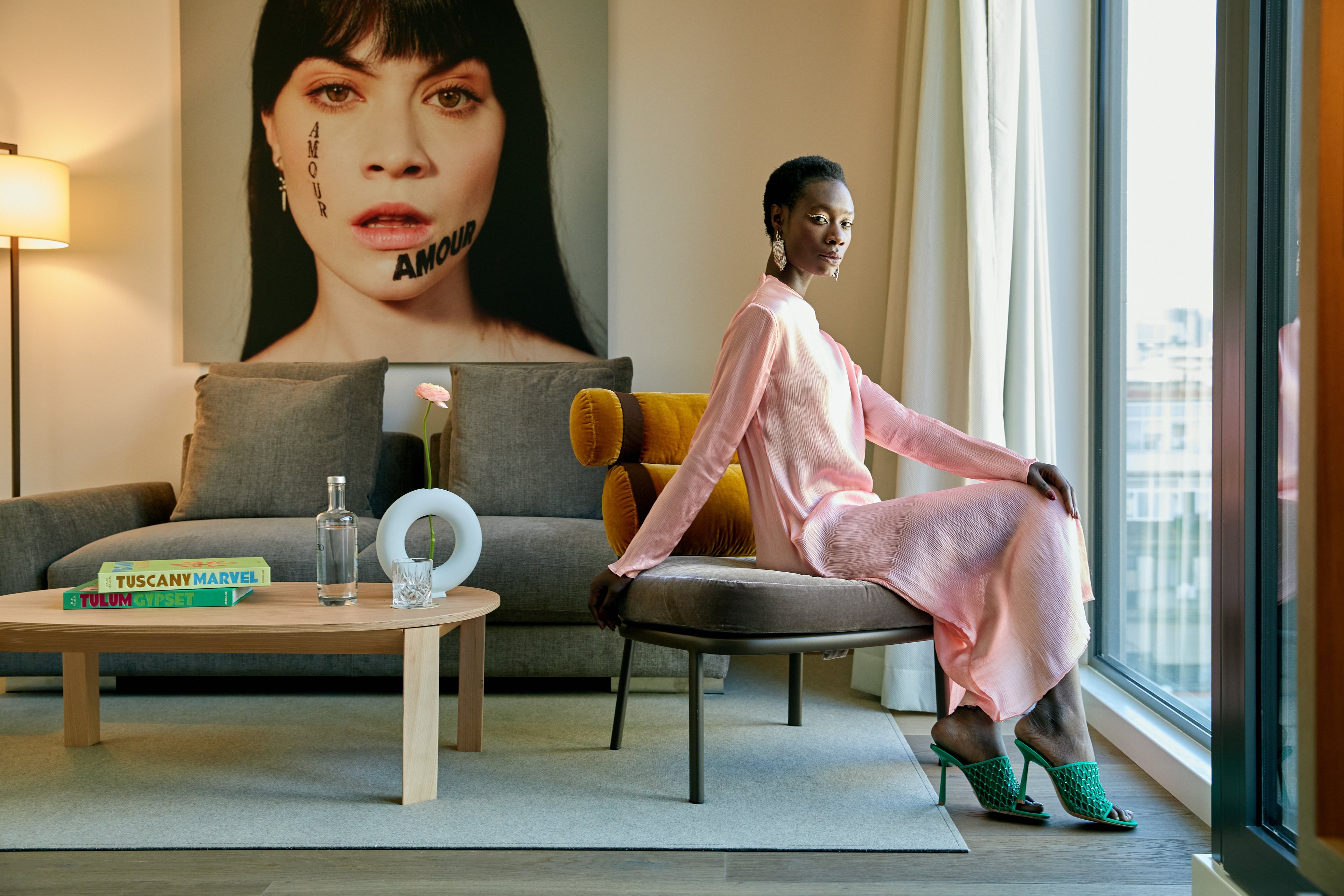 Contemporary elegance meets artistic flair in this sun-drenched living space, where coral-pink silk draping and emerald accessories create an unexpectedly sophisticated palette against Barcelona's urban backdrop.
