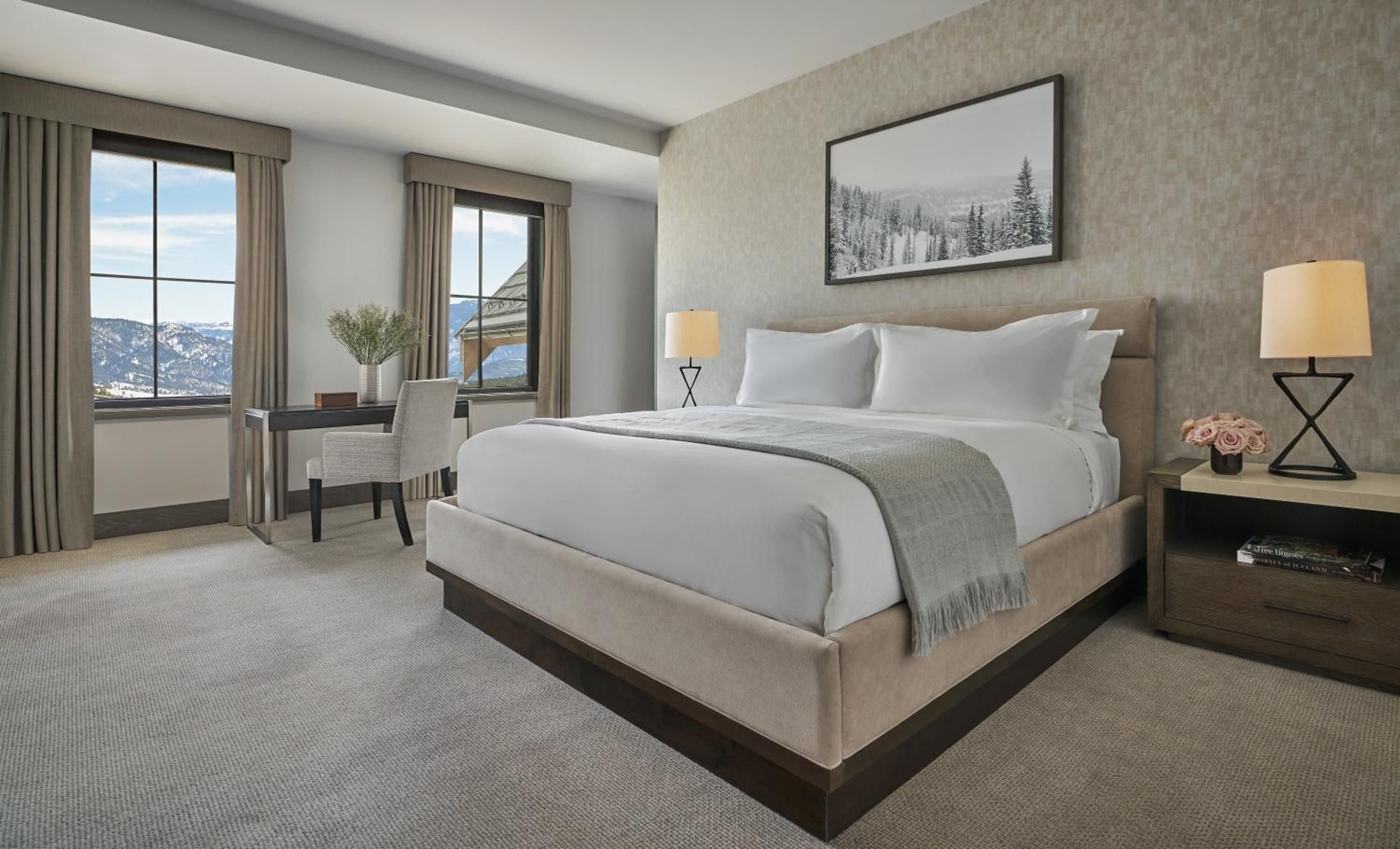 Soft taupe tones and crisp white linens create a serene retreat, while floor-to-ceiling windows frame dramatic mountain vistas beyond the thoughtfully appointed king suite.