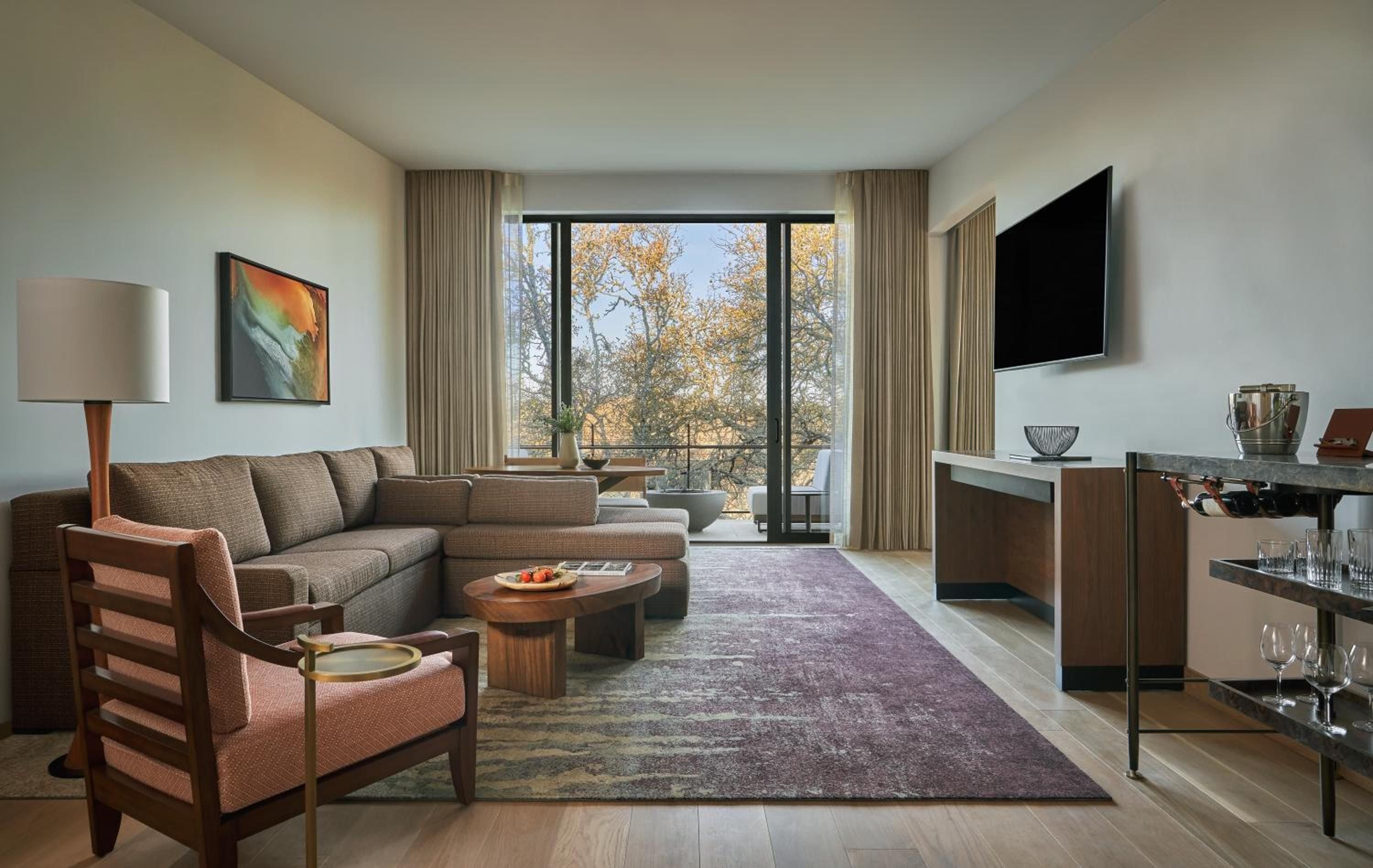 Floor-to-ceiling windows frame golden autumn foliage while warm walnut and purple accents create an inviting living space that seamlessly blends Sonoma's natural beauty with sophisticated comfort.