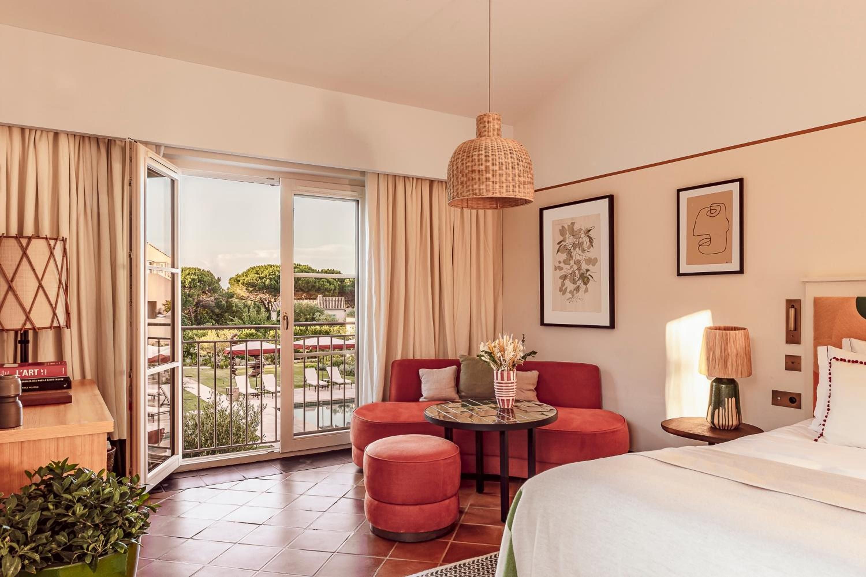 Terracotta walls and coral velvet seating create intimate warmth in this thoughtfully designed suite, where rattan pendants cast gentle shadows and French doors frame Mediterranean views.