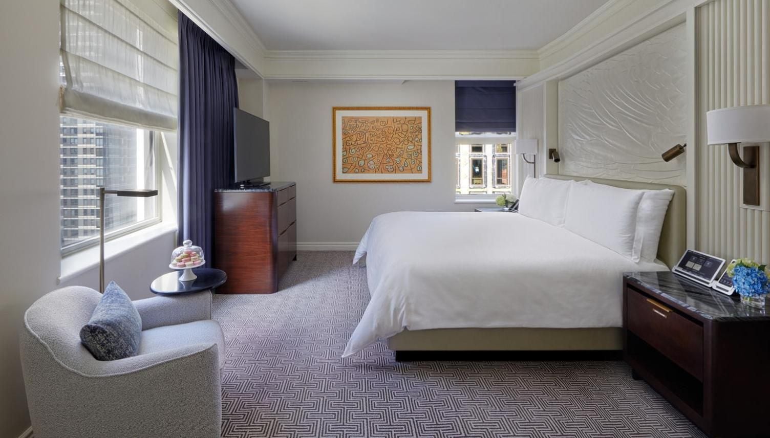 Crisp white linens contrast beautifully with rich mahogany furnishings and geometric carpeting, while floor-to-ceiling windows frame Manhattan's architectural tapestry beyond.