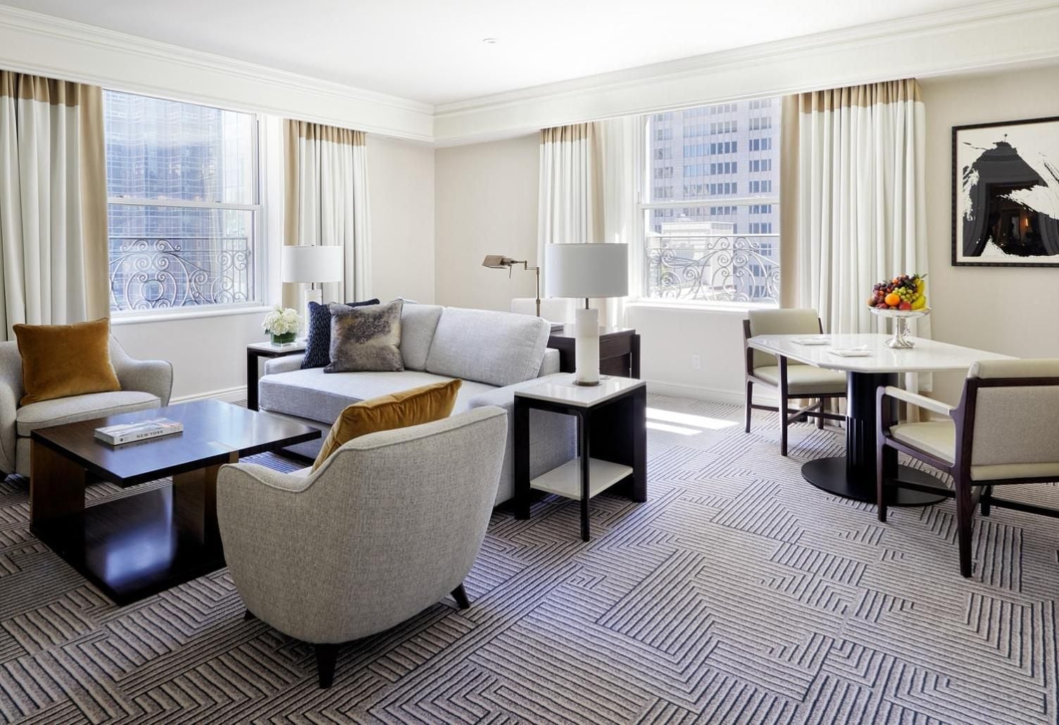 Corner windows flood the elegant suite with Manhattan light, while geometric carpeting and honey-toned accents create sophisticated warmth against neutral furnishings.