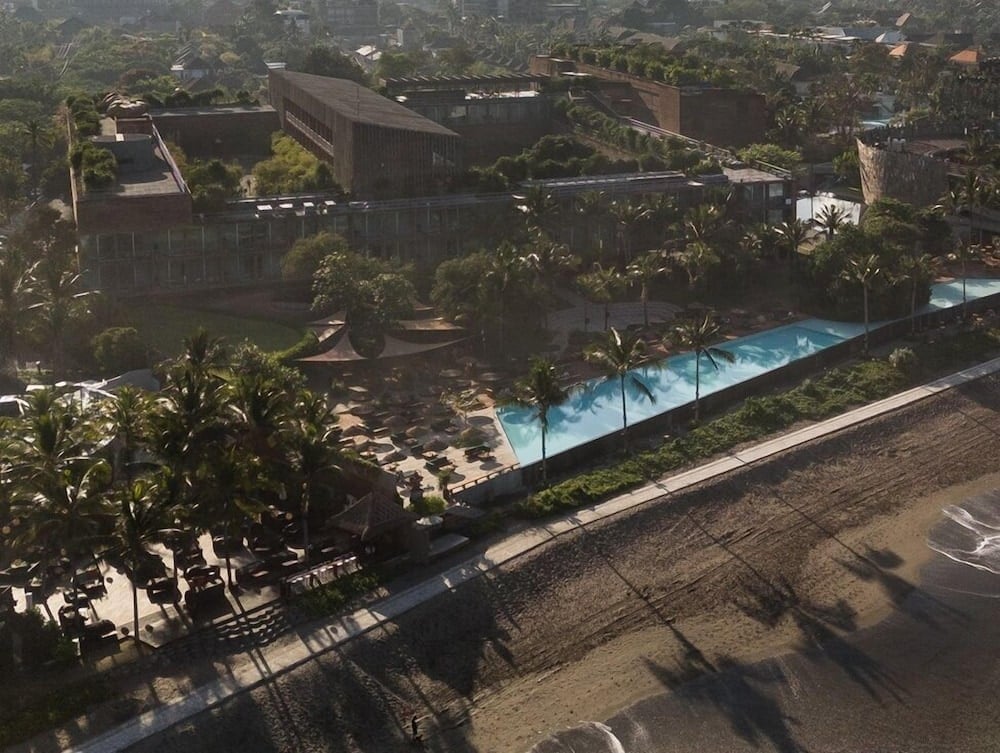 Palm shadows stretch across the infinity pool's turquoise expanse while Desa Potato Head's striking angular architecture rises from Bali's lush tropical canopy.