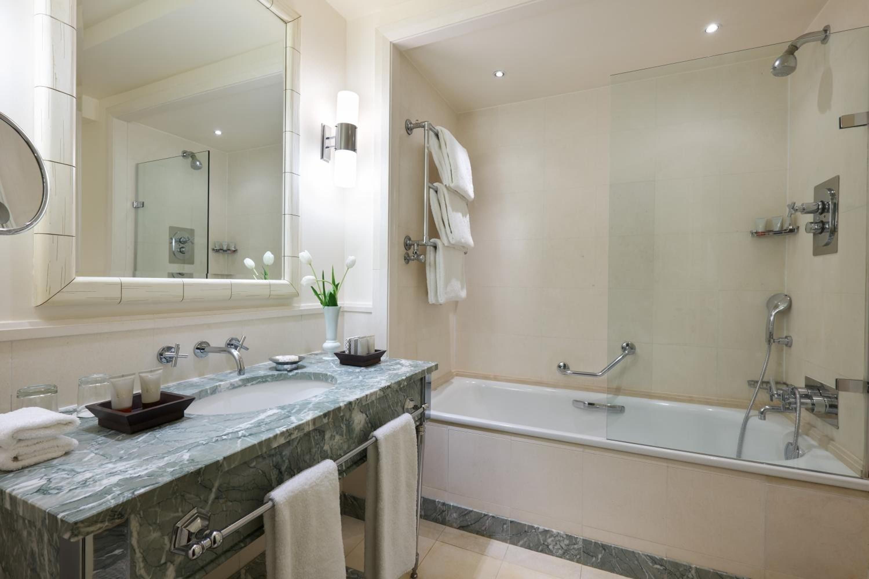 Gleaming marble countertops and warm limestone walls create a spa-like sanctuary, where crisp white towels and soft lighting invite luxurious soaking rituals.