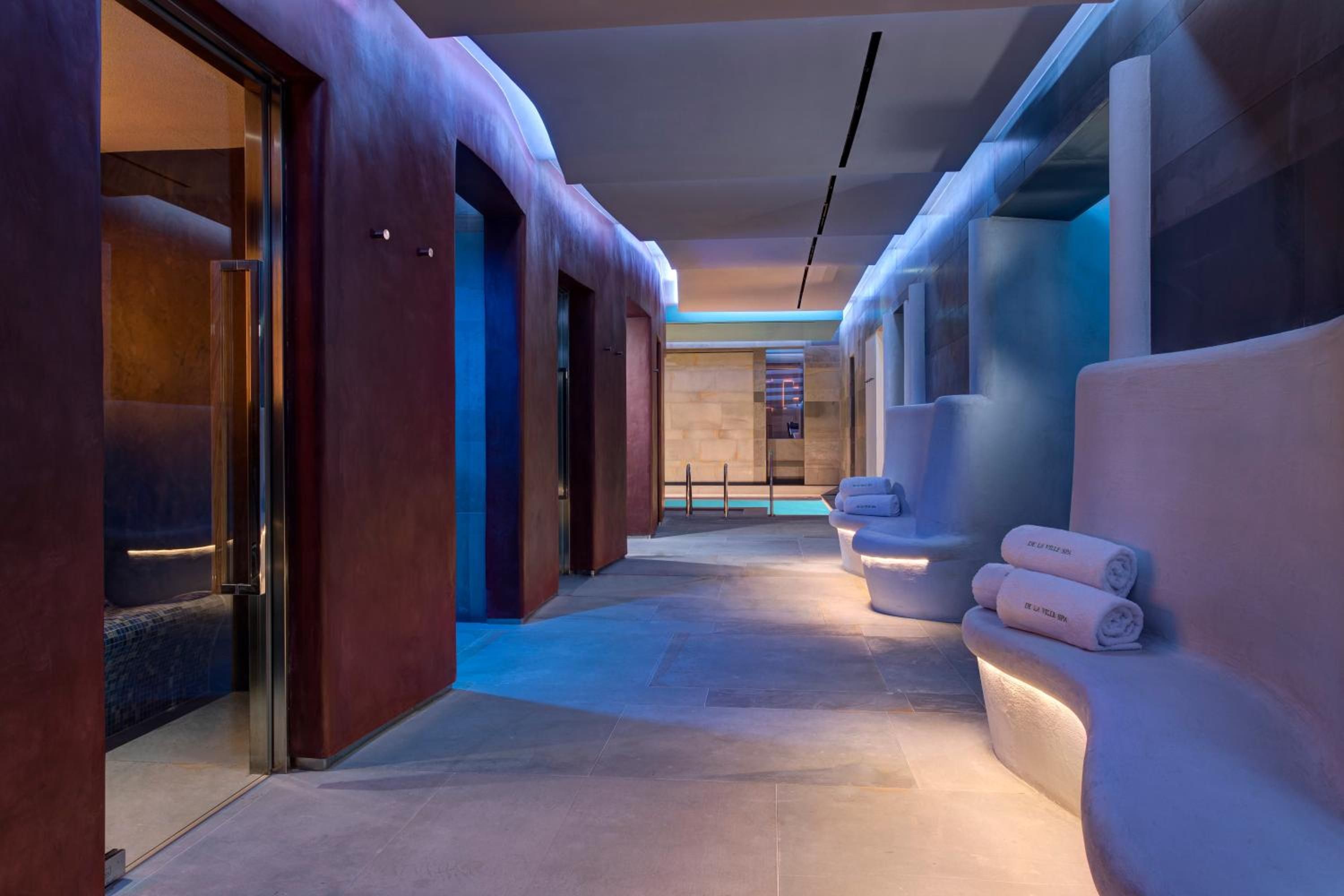 Curved alcoves carved from white stone house plush towels along this ethereal spa corridor, where soft blue lighting creates an underwater grotto atmosphere.