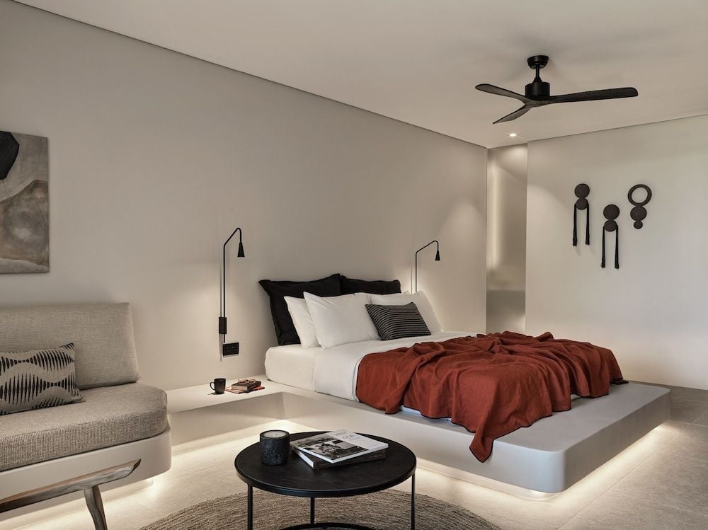 Minimalist elegance defines this floating platform bed, where warm terracotta linens contrast beautifully against cool concrete surfaces and sculptural wall art creates intimate ambiance.