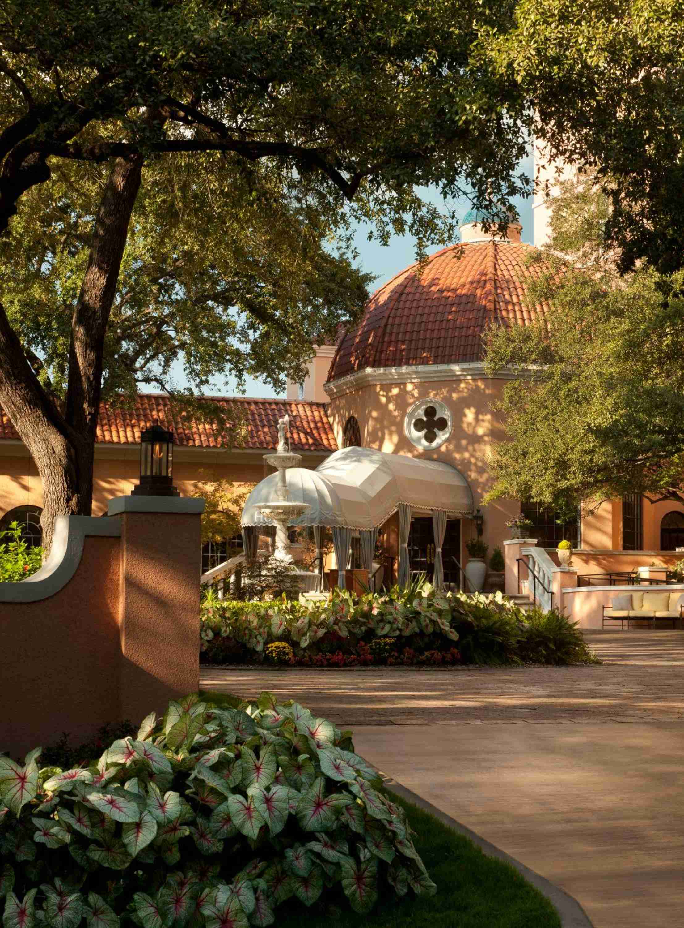 Dappled sunlight filters through mature oaks onto the mansion's Mediterranean-inspired rotunda, where clay tiles gleam above manicured caladium beds and stone pathways.