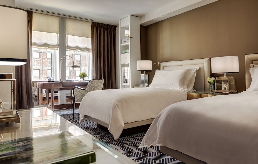 Twin beds dressed in crisp white linens anchor this sophisticated guest room, where geometric carpets and warm taupe walls create an intimate Upper East Side sanctuary.